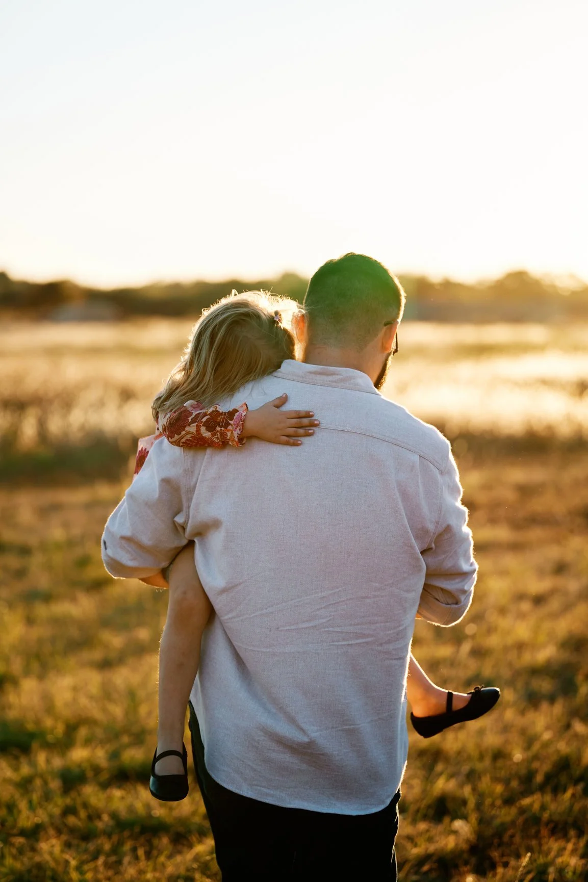 Golden hour outdoor dad holding daughter walking through field.jpg