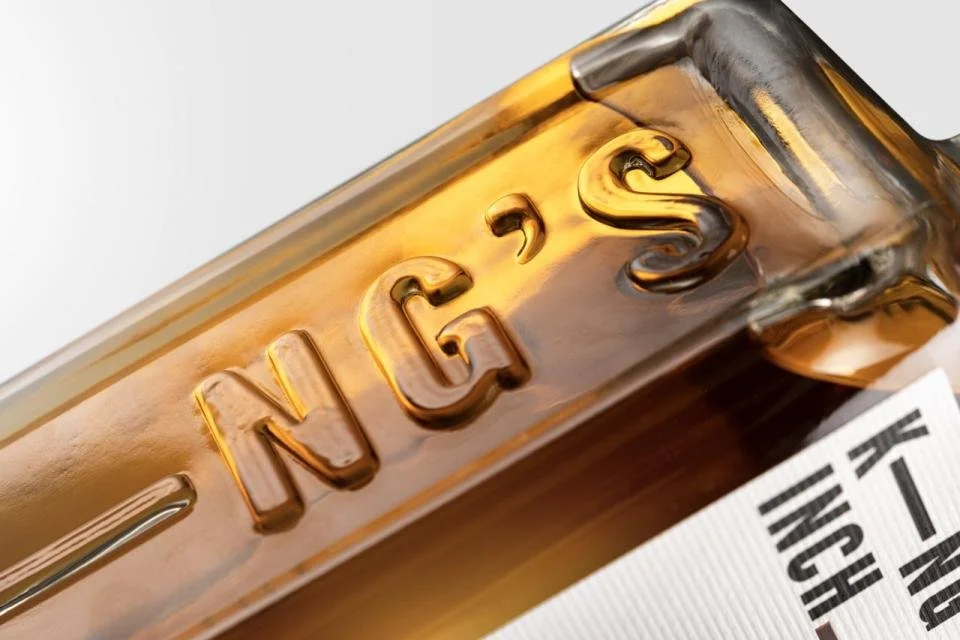 Close-up of a King's Inch Whisky bottle with the word "King's" embossed on it, containing a golden liquid.