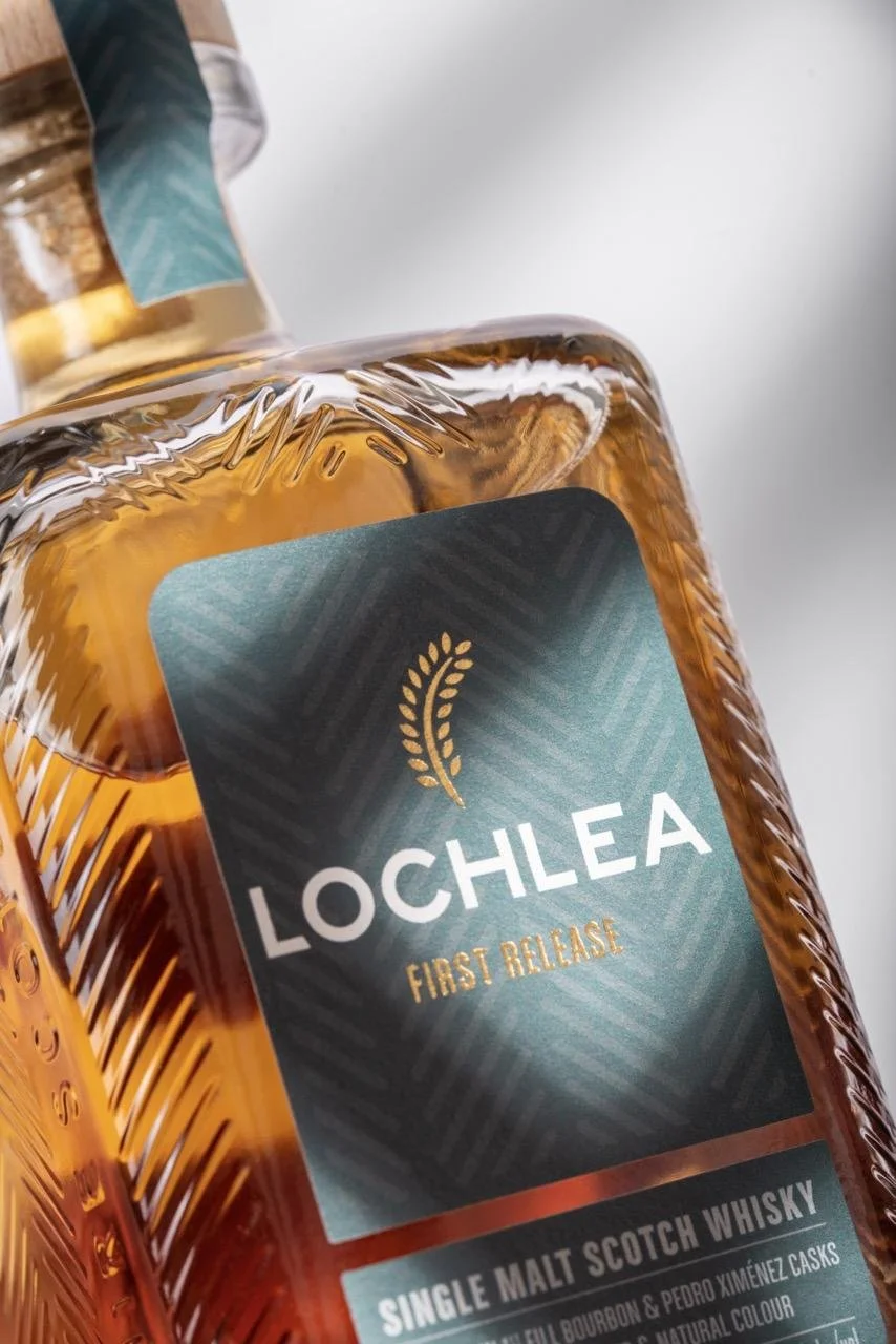 Close-up of a bottle of Lochlea single malt scotch whisky with a label that reads 'First Release,' featuring a teal and black design with a gold leaf icon.
