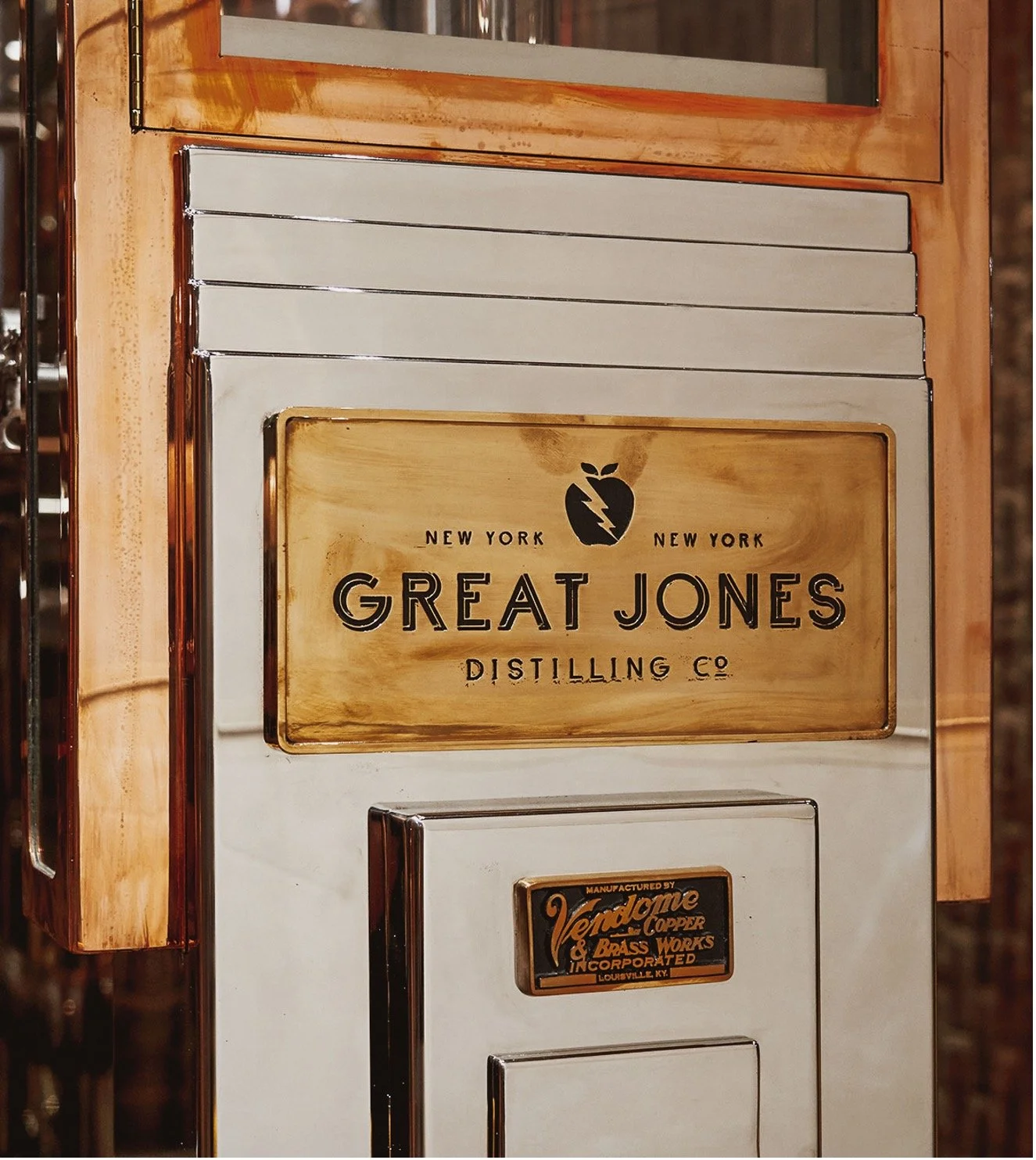 Vintage style spirits safe with a copper sign for Great Jones Distilling Co., featuring a logo with a lightning bolt inside a apple shape, and a smaller label for Vendome Copper & Brass Works Inc. Louisville, KY.