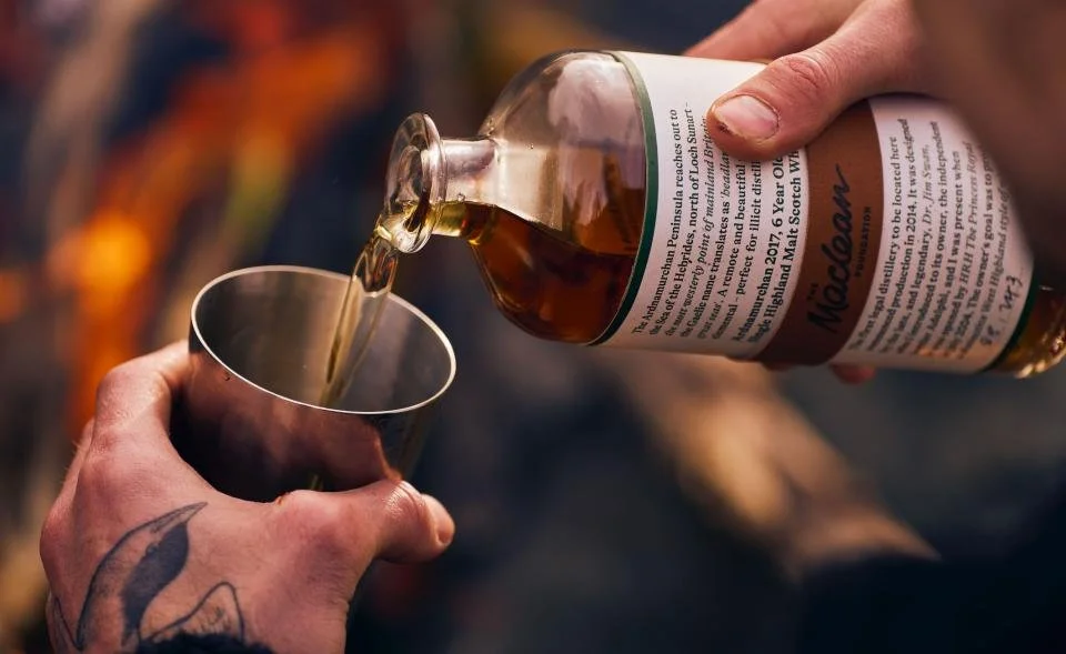 Person pouring Maclean Foundation whisky from a bottle into a metal cup.