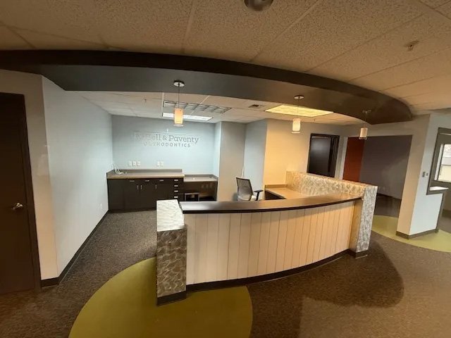 Reception area with a curved counter, office chair, and a sign reading 'Russell & Paventy Orthodontics' on the wall behind the counter.