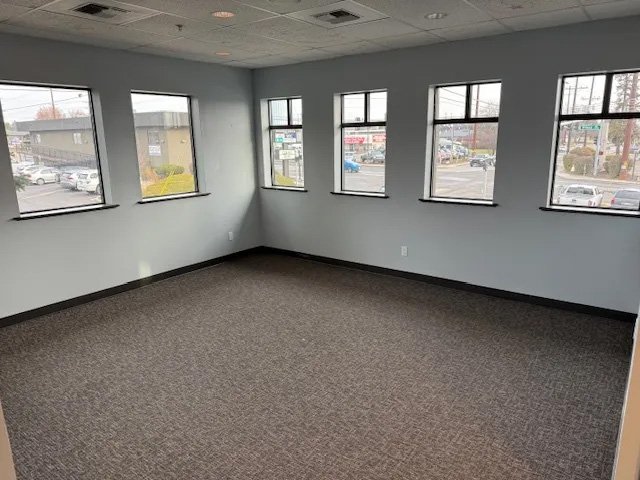 Empty office room with five large windows, gray walls, and dark carpet flooring.