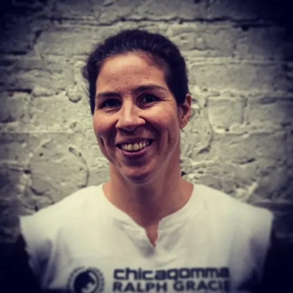 Woman smiling in front of a brick wall, wearing a white shirt with text that reads 'chicago marathon, Ralph Grace'.