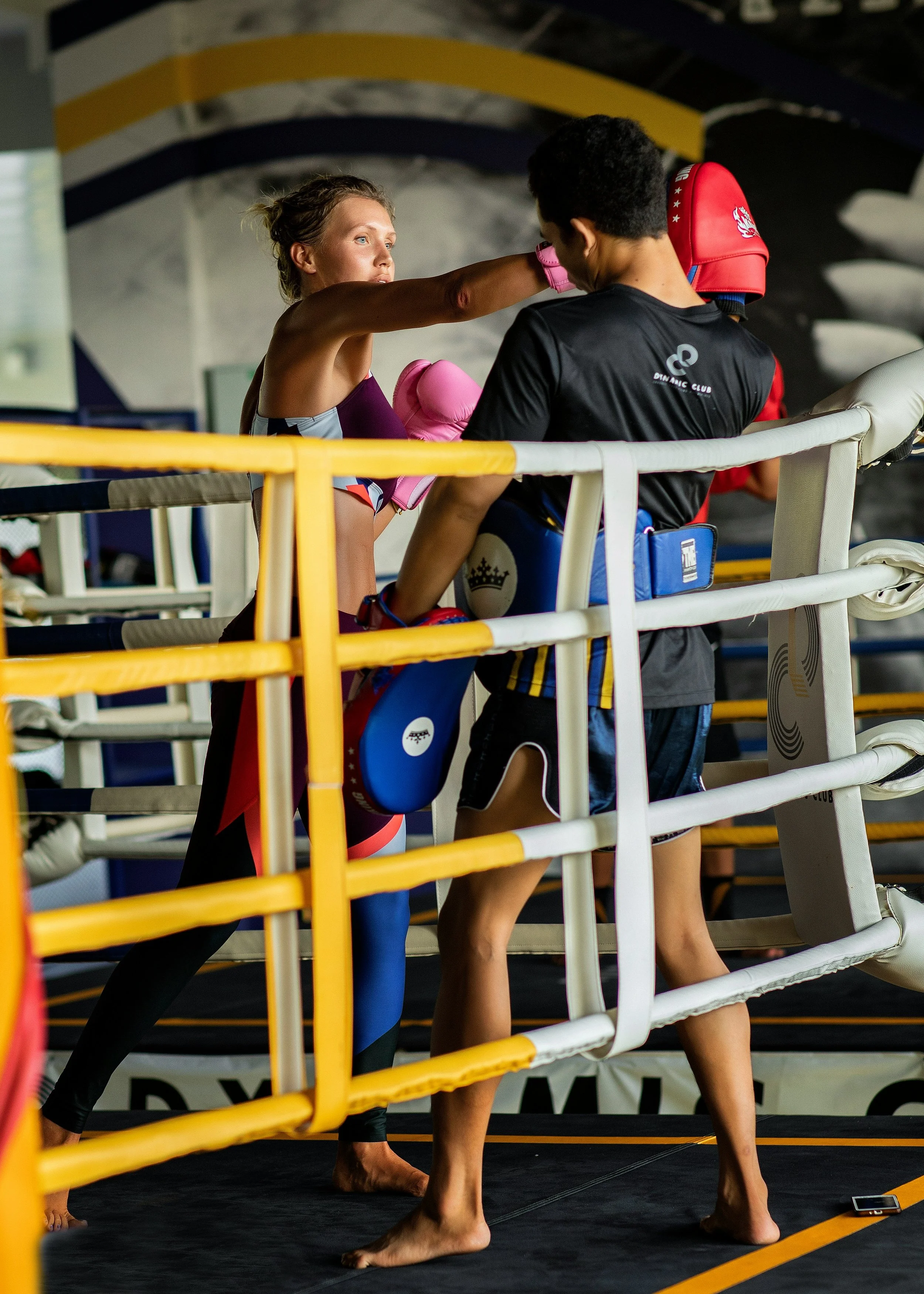 A female martial artist practicing punches on a male instructor in a boxing ring, with the instructor holding focus pads.