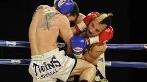 Two female fighters in a boxing match inside a ring, one wearing red gloves and the other wearing blue gloves, engaged in a close-up moment.