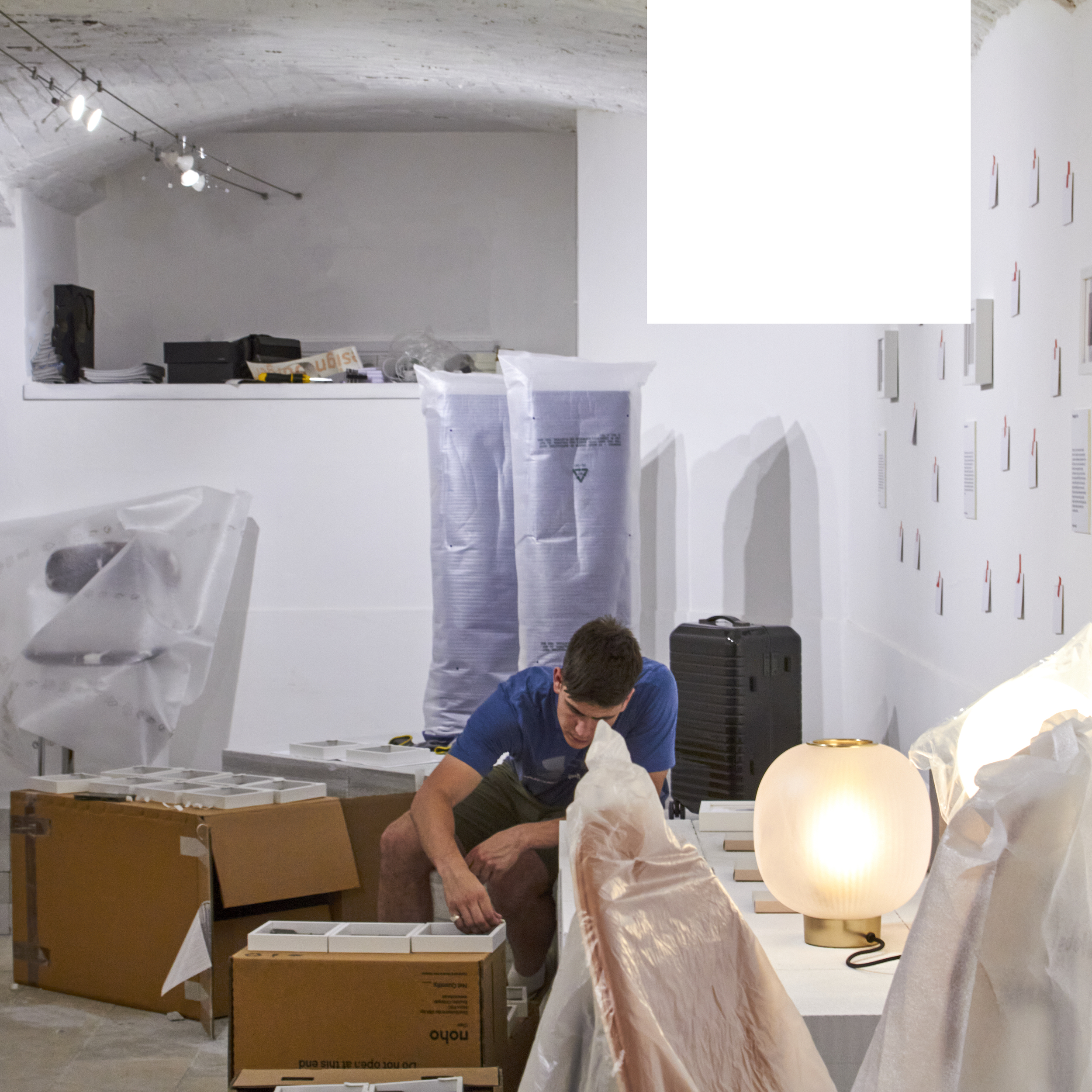 Team unwrapping products and placing dust-covered designer pieces on the floor in preparation for the Design Dialogues Exhibition in Isola District, Milan.