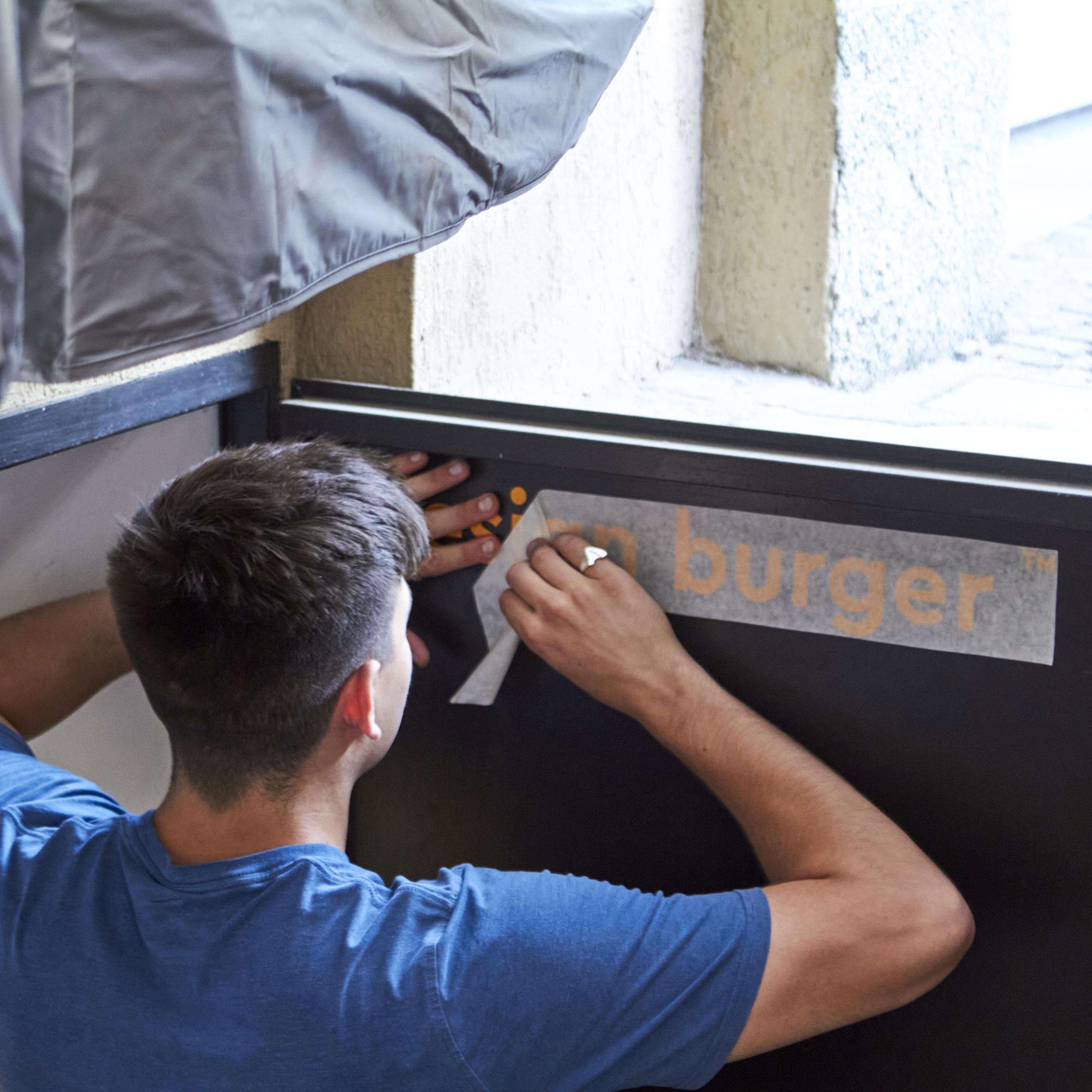 Team member peeling off a wall decal from a black door during exhibition setup, showing the attention to detail in gallery branding.