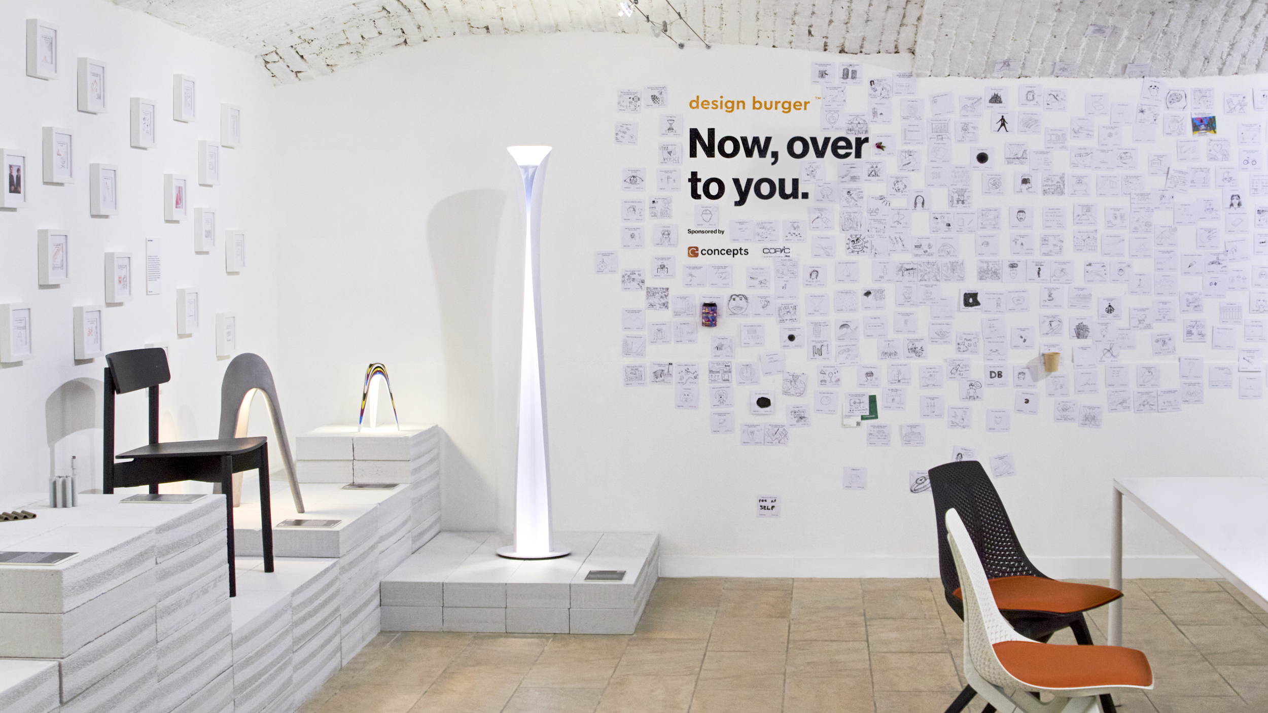 Wide shot of the large interactive wall at the exhibition covered with guest sketches, next to a Karim Rashid floor lamp.