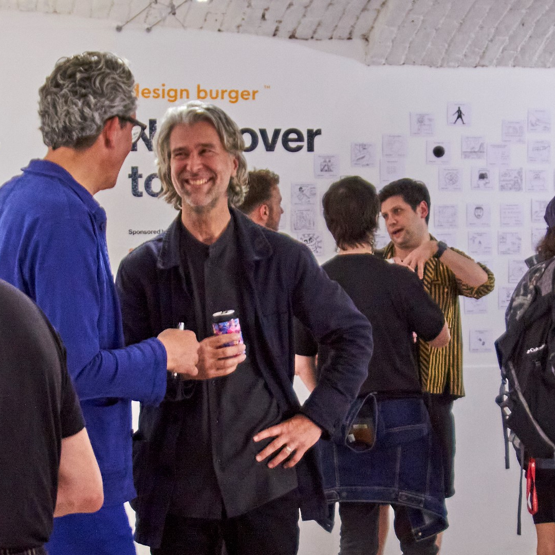 Luke Pearson engaged in conversation with Sebastian Bergne at the exhibition opening, with attendees in the background.