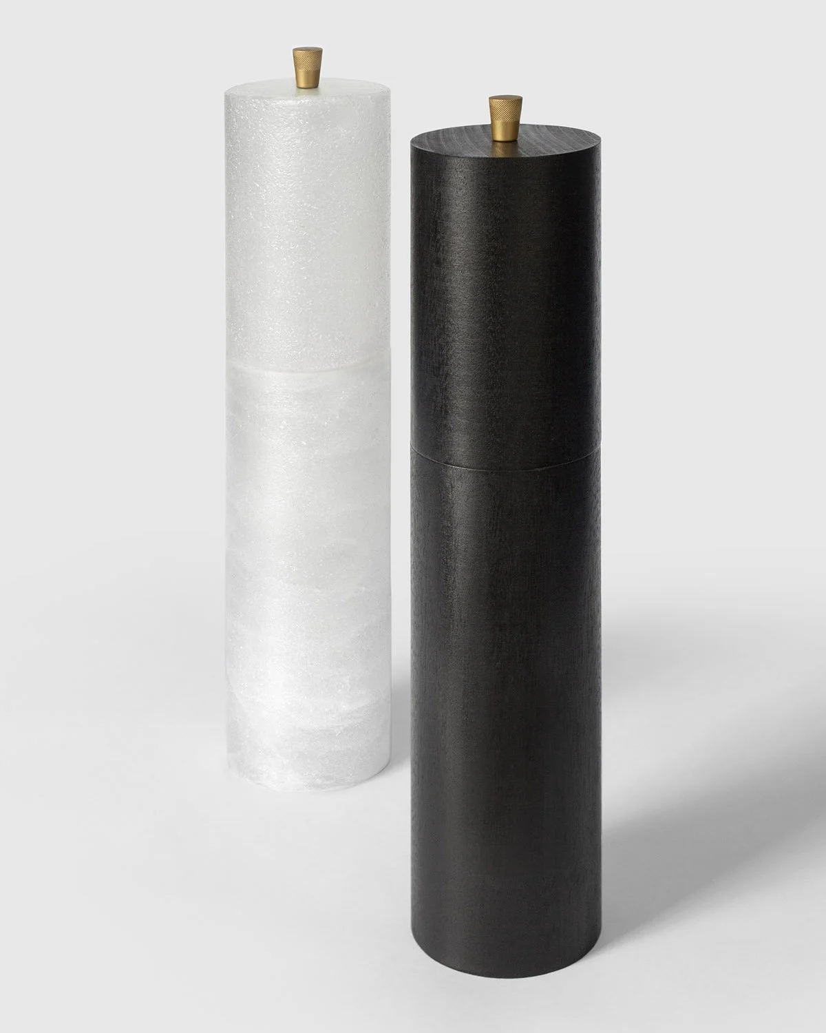 Three-quarter studio view of Origin Salt and Pepper Mills, black pepper version in front, showcasing contrast of natural materials in minimalist form.
