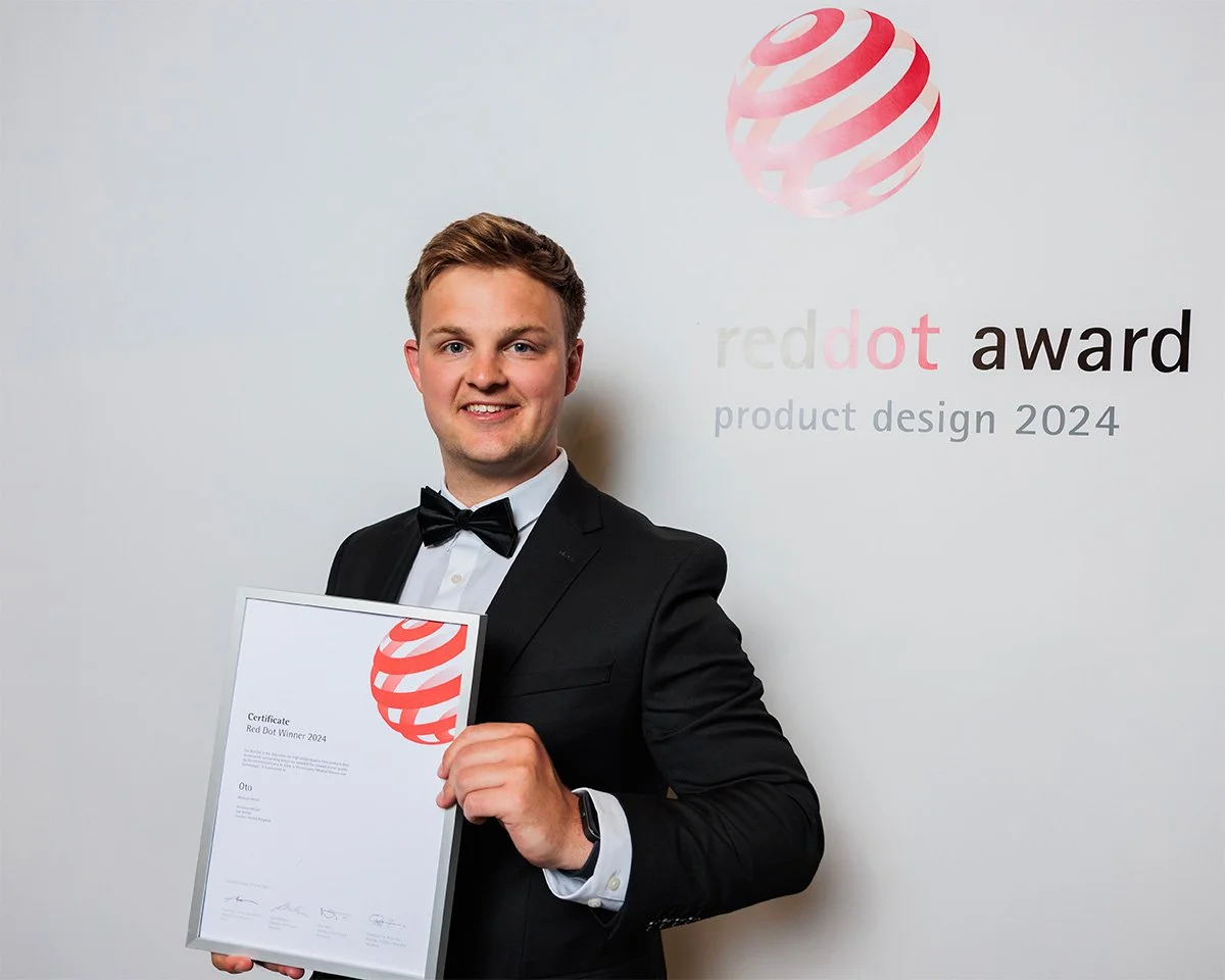 Designer Joe Slatter in a black tuxedo and bow tie holding a certificate at the Red Dot Design Award.