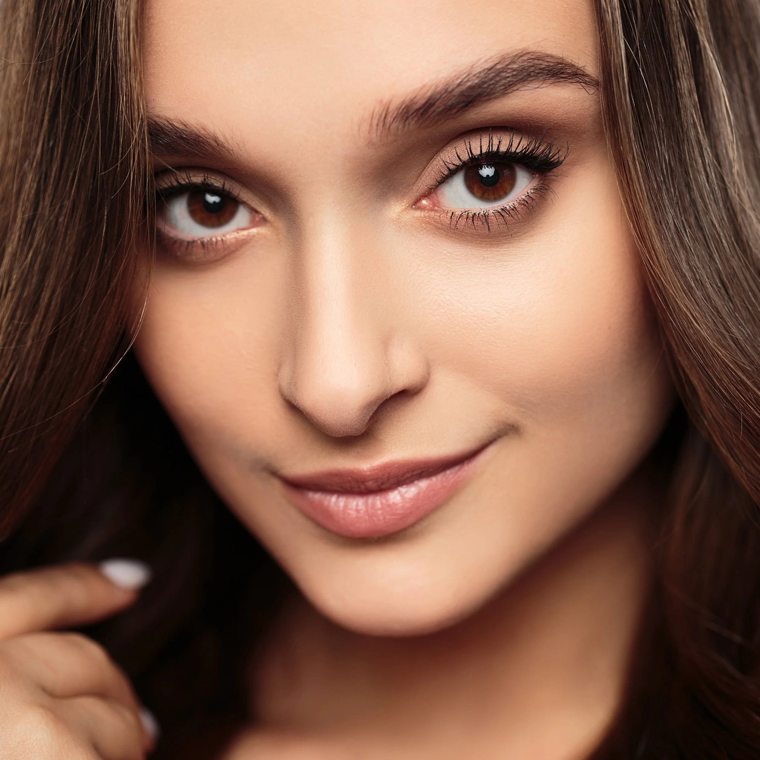Close-up portrait of a woman with brown eyes and long brown hair, smiling softly.