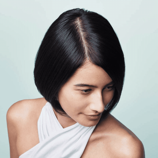 Close-up of a woman with black, straight, shoulder-length hair, wearing a white sleeveless top, looking down.