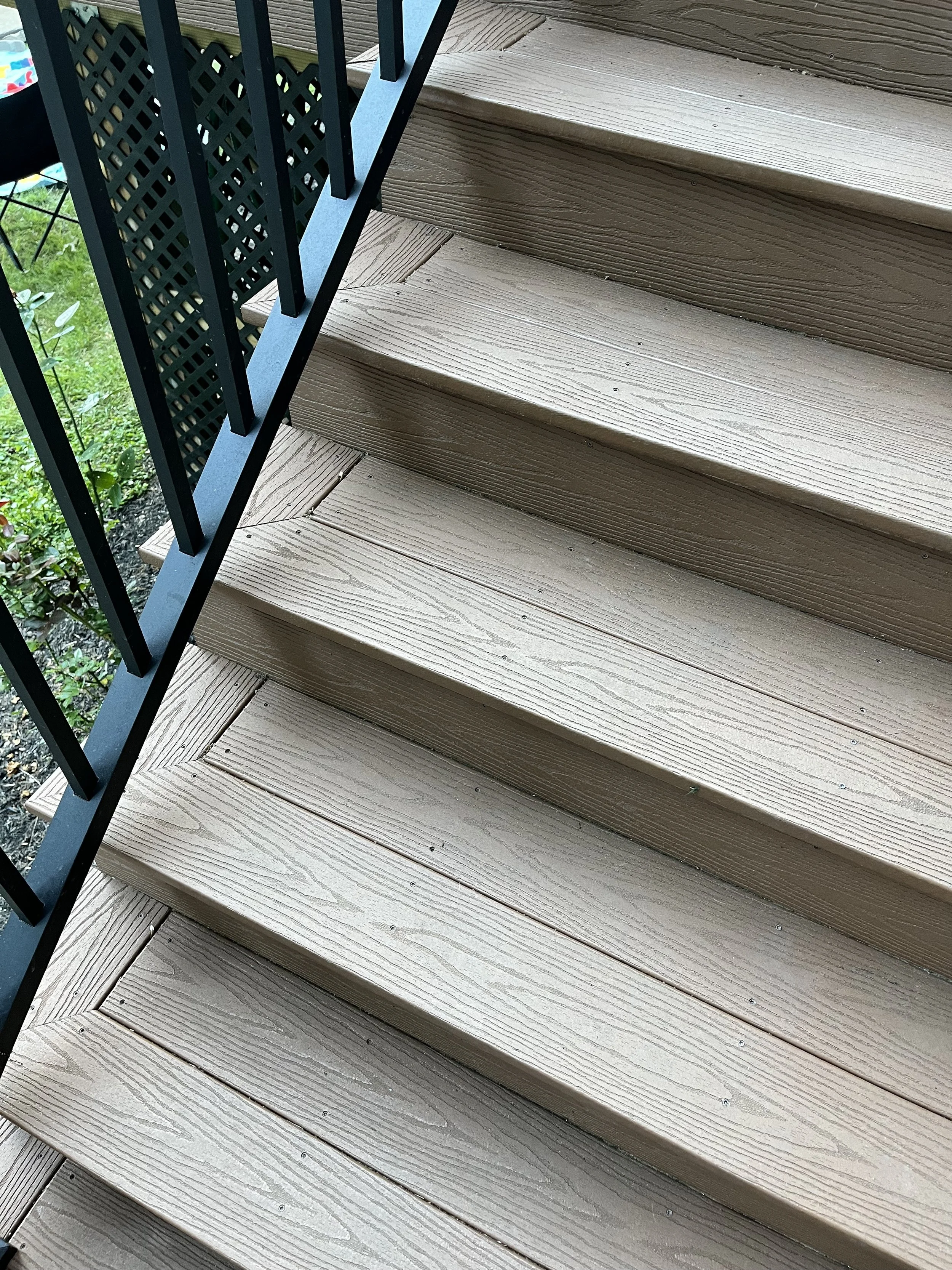 Wooden stairs with metal railing on the left side in an outdoor setting.
