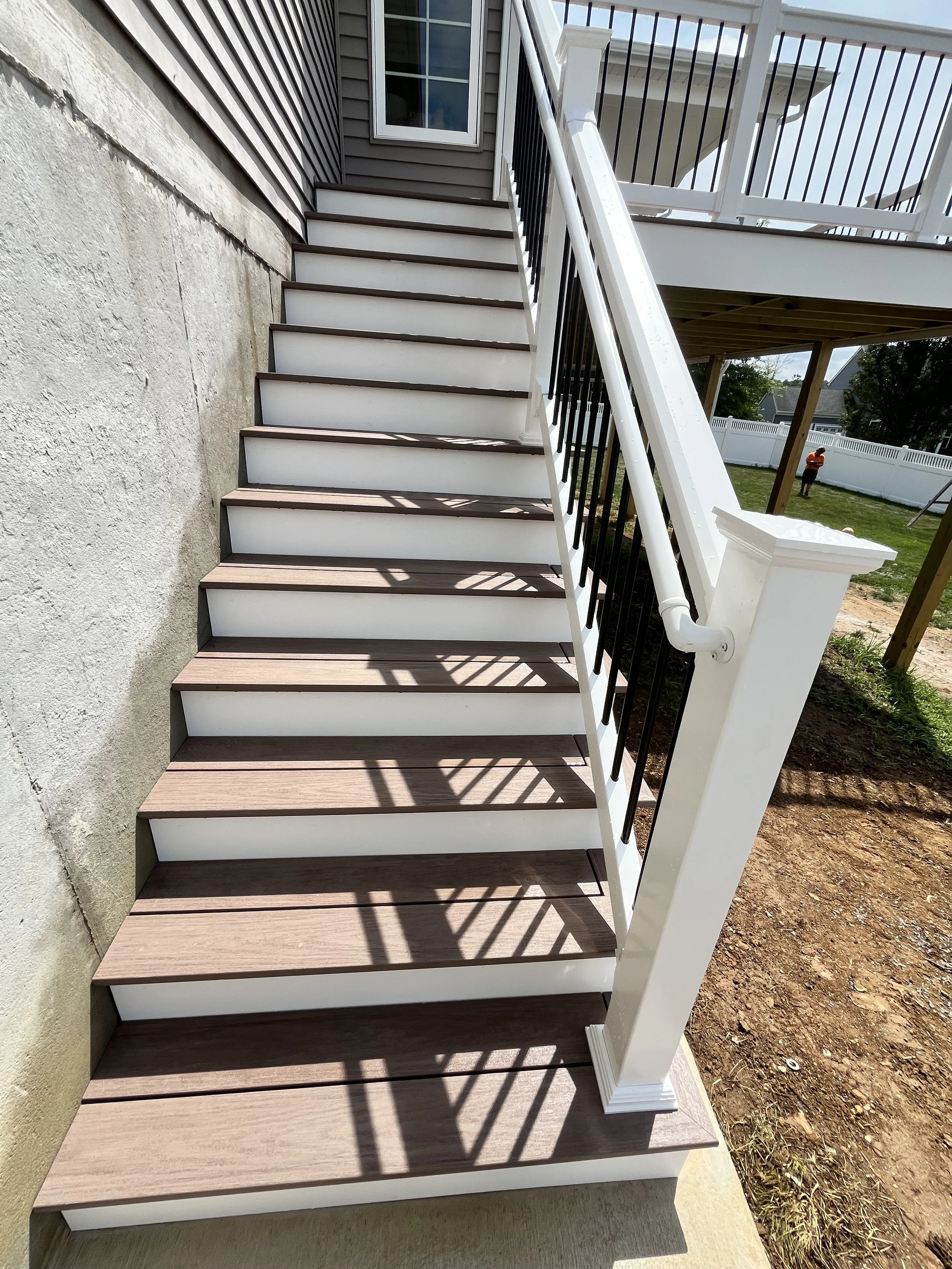 The image shows a staircase with wood steps and a black and white railing, leading to a second-story porch outside a house with dark gray siding.