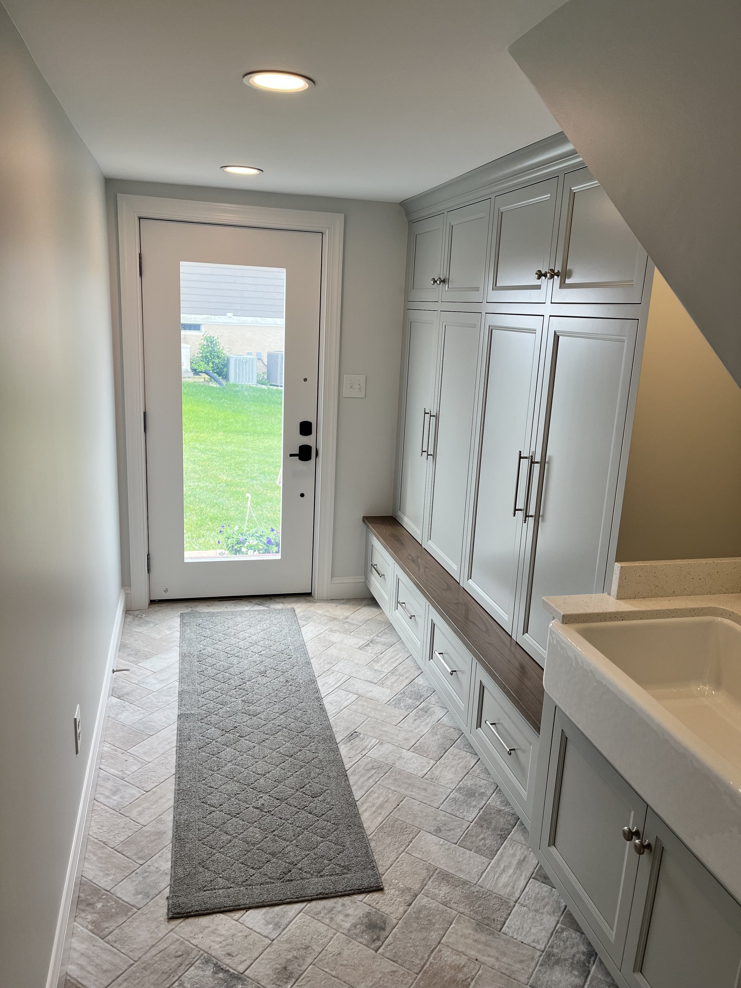 Entryway with a gray cabinet, white walls, tiled floor, a gray rug, and a glass back door leading outside to a green lawn.