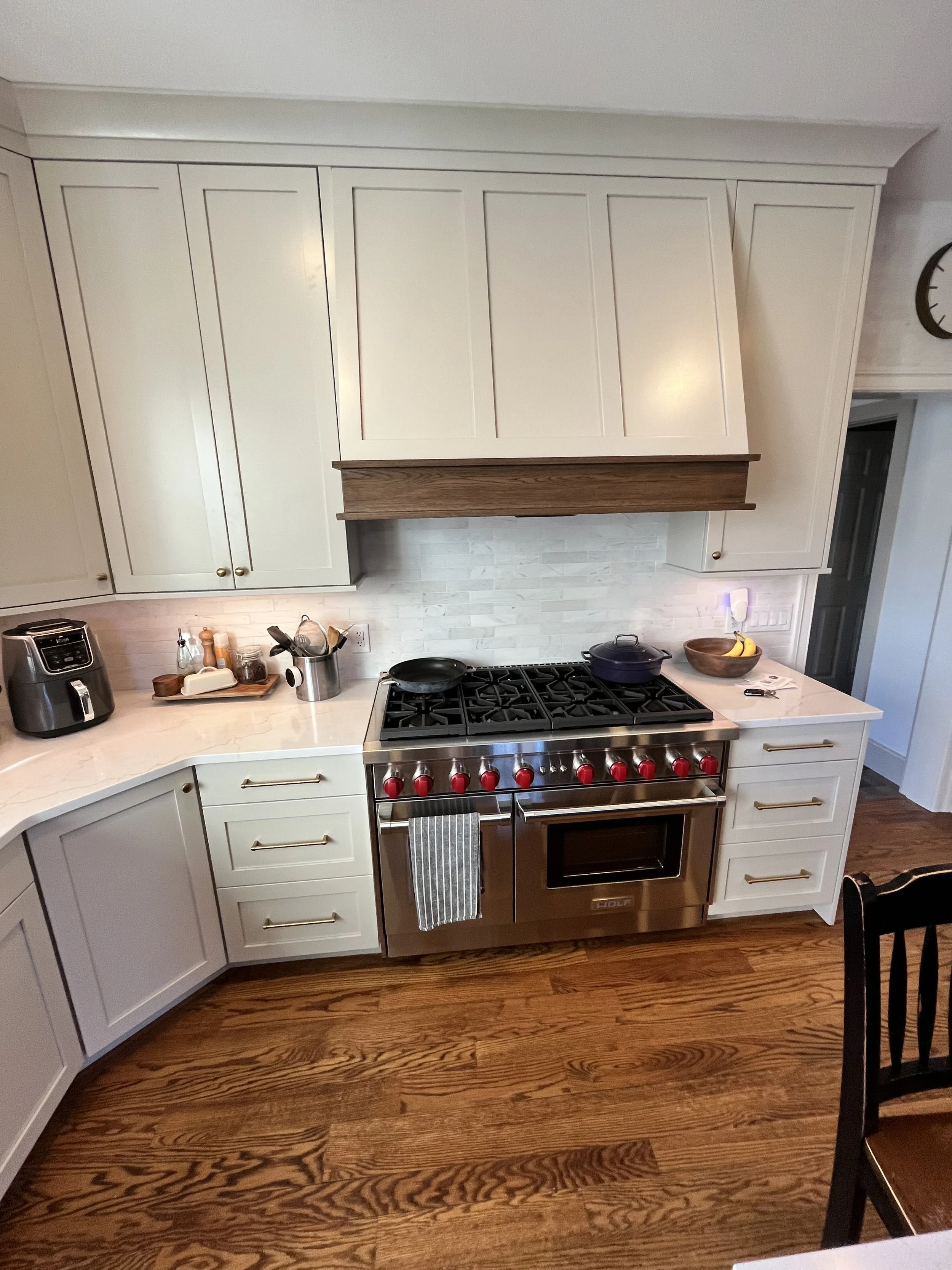 A kitchen with white cabinets, a stove, a wooden countertop, and various kitchen items including a bowl of bananas, a French press, and a toaster.
