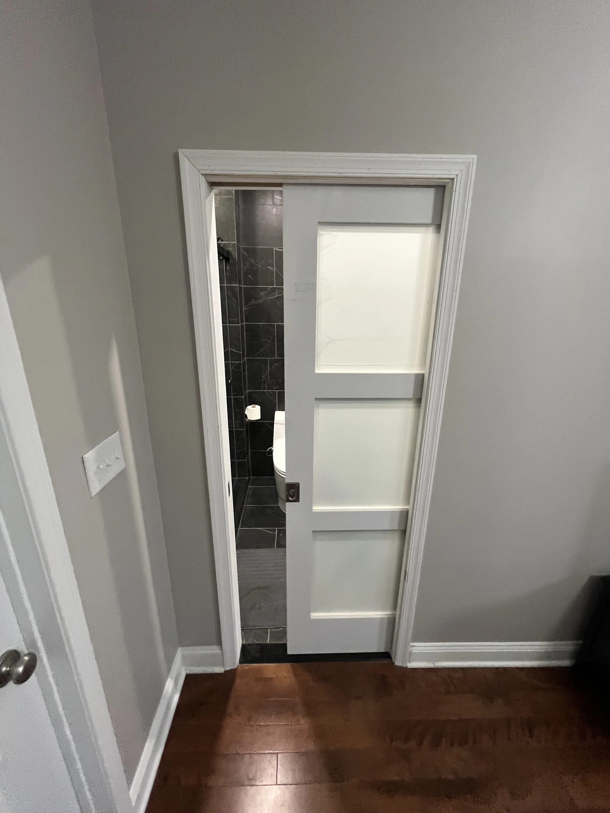 A white sliding door partially open, revealing a black tiled bathroom with a toilet inside.