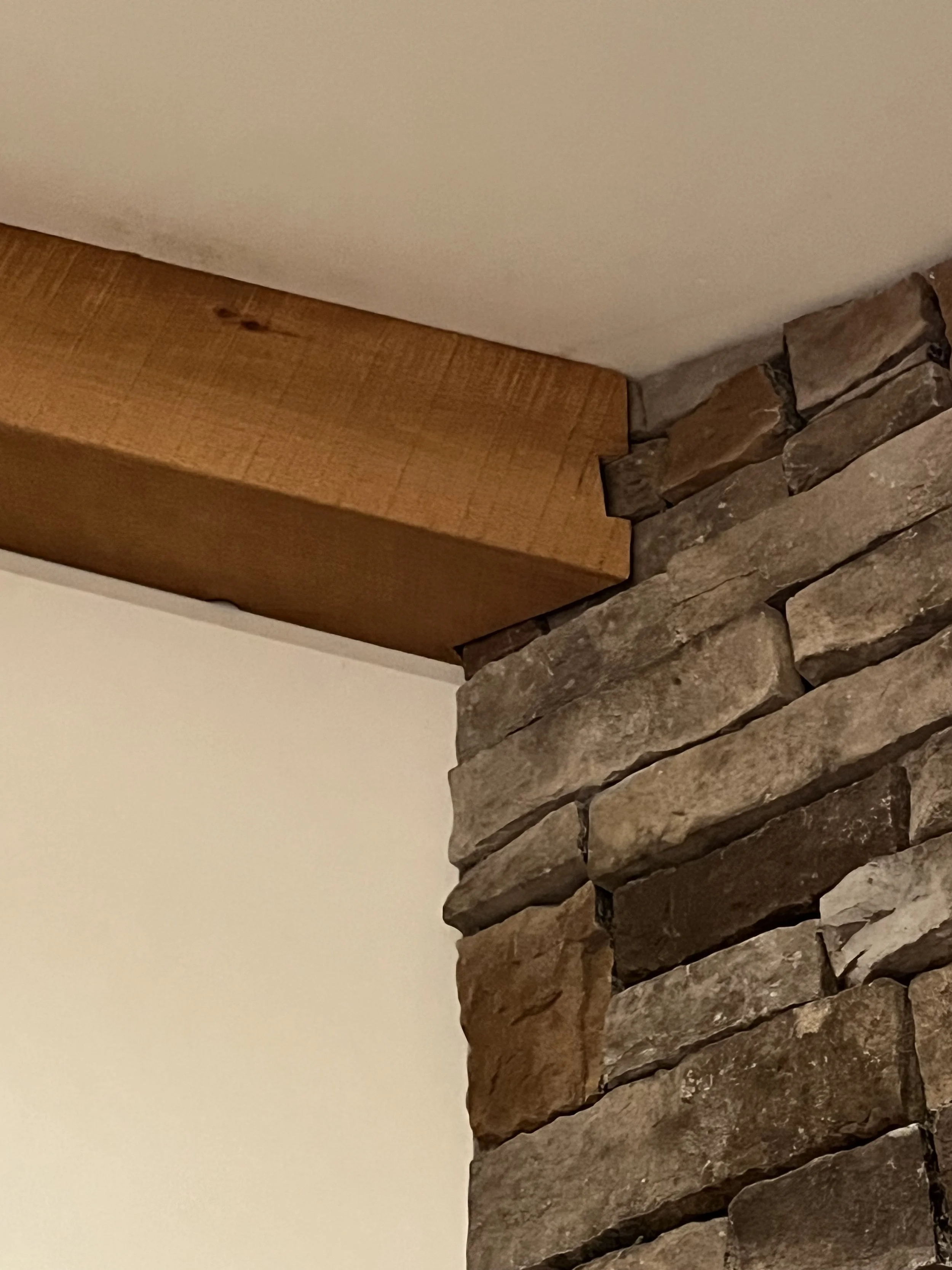 Close-up of a corner with a wooden beam and stacked stone wall against a plain white wall.