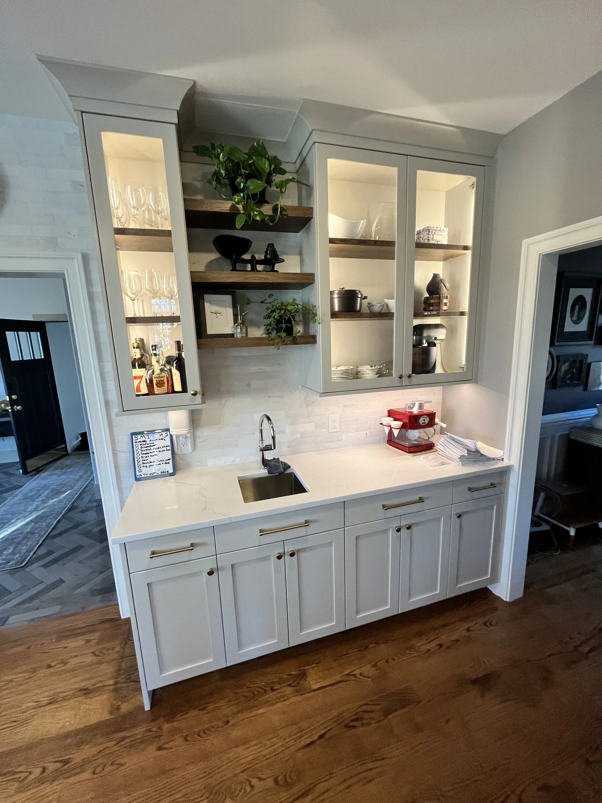 Kitchen with white cabinetry, open shelves with glassware and decorative items, white countertops, and hardwood floors.