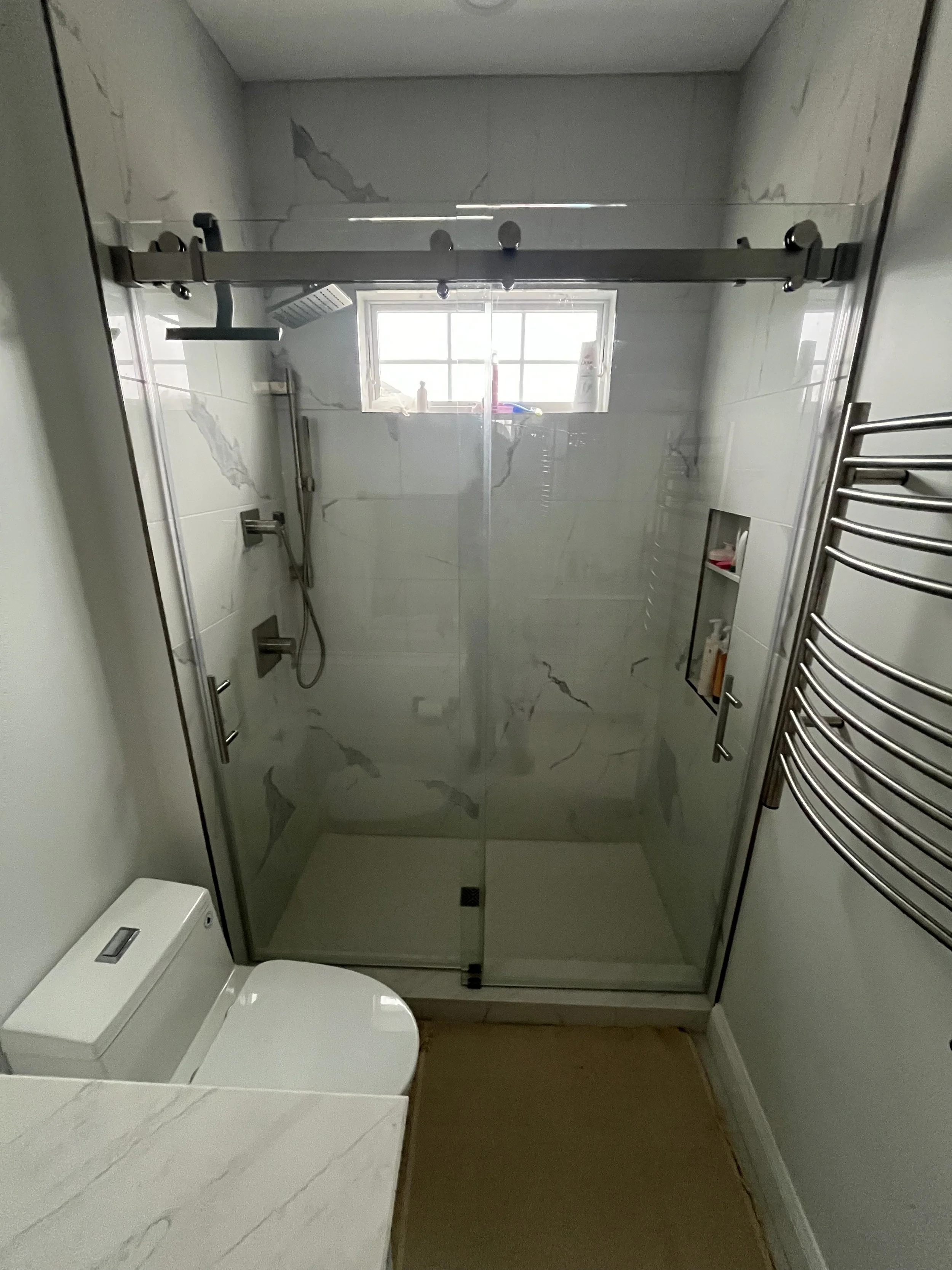 Modern bathroom with shower, white marble walls, window, heated towel rack, and toilet.