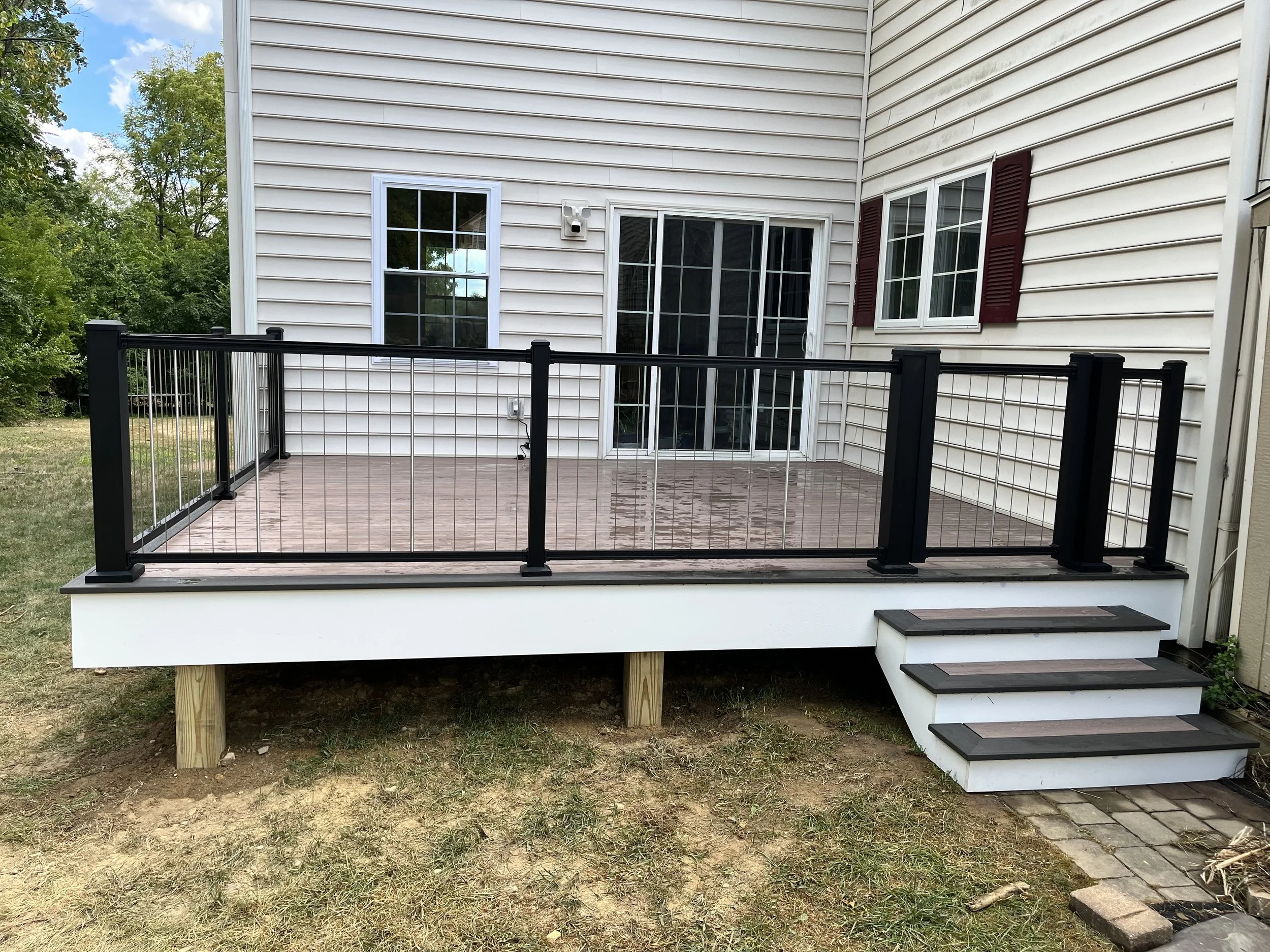 Backyard deck with sliding glass door, two windows with red shutters, and a security camera on the house exterior.