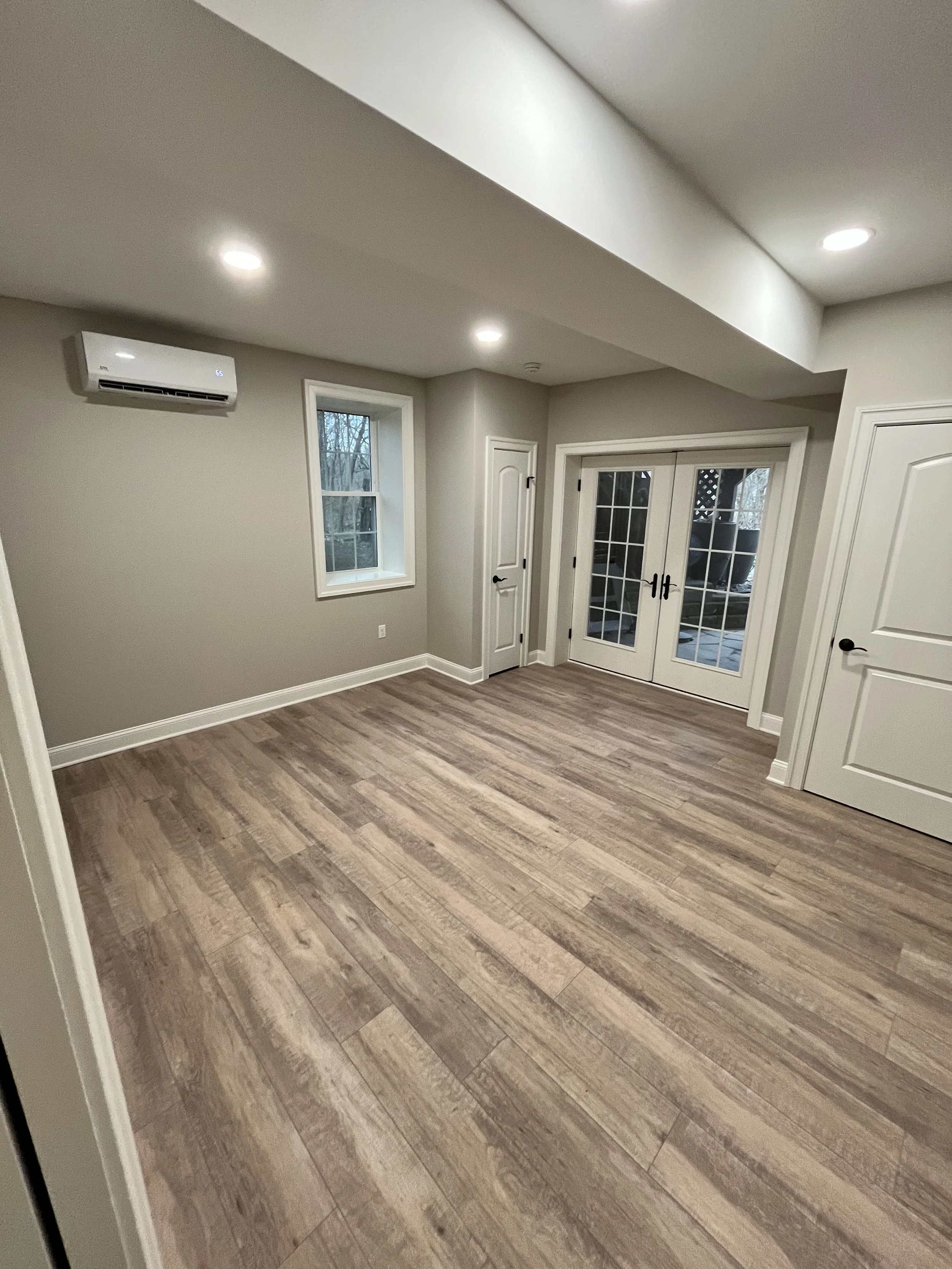 Interior room with wooden flooring, beige walls, white doors, a small window, a sliding glass door leading outside, and recessed ceiling lights.
