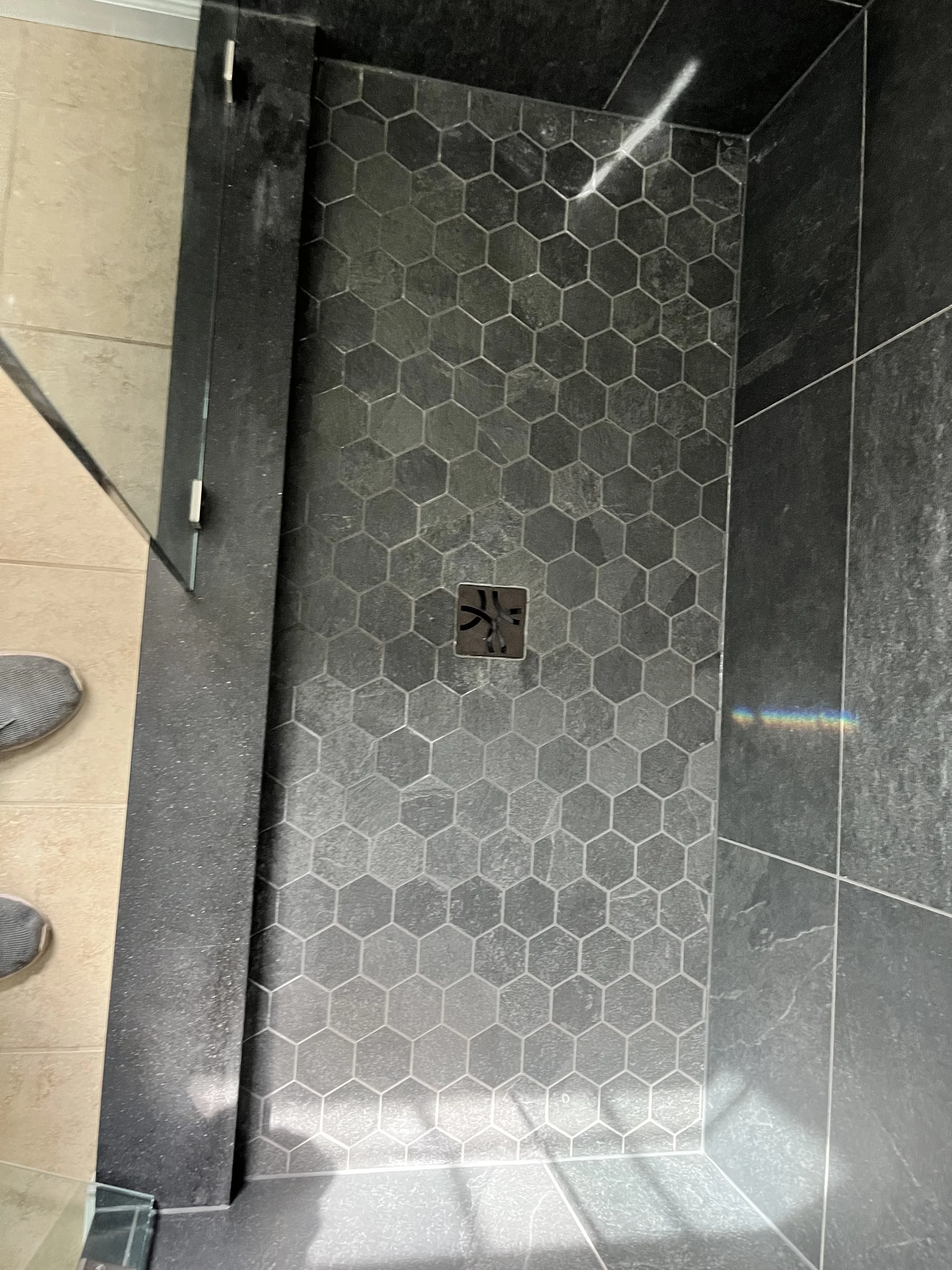Shower area with black hexagonal tiles on the floor and black wall tiles, with a floor drain in the center.