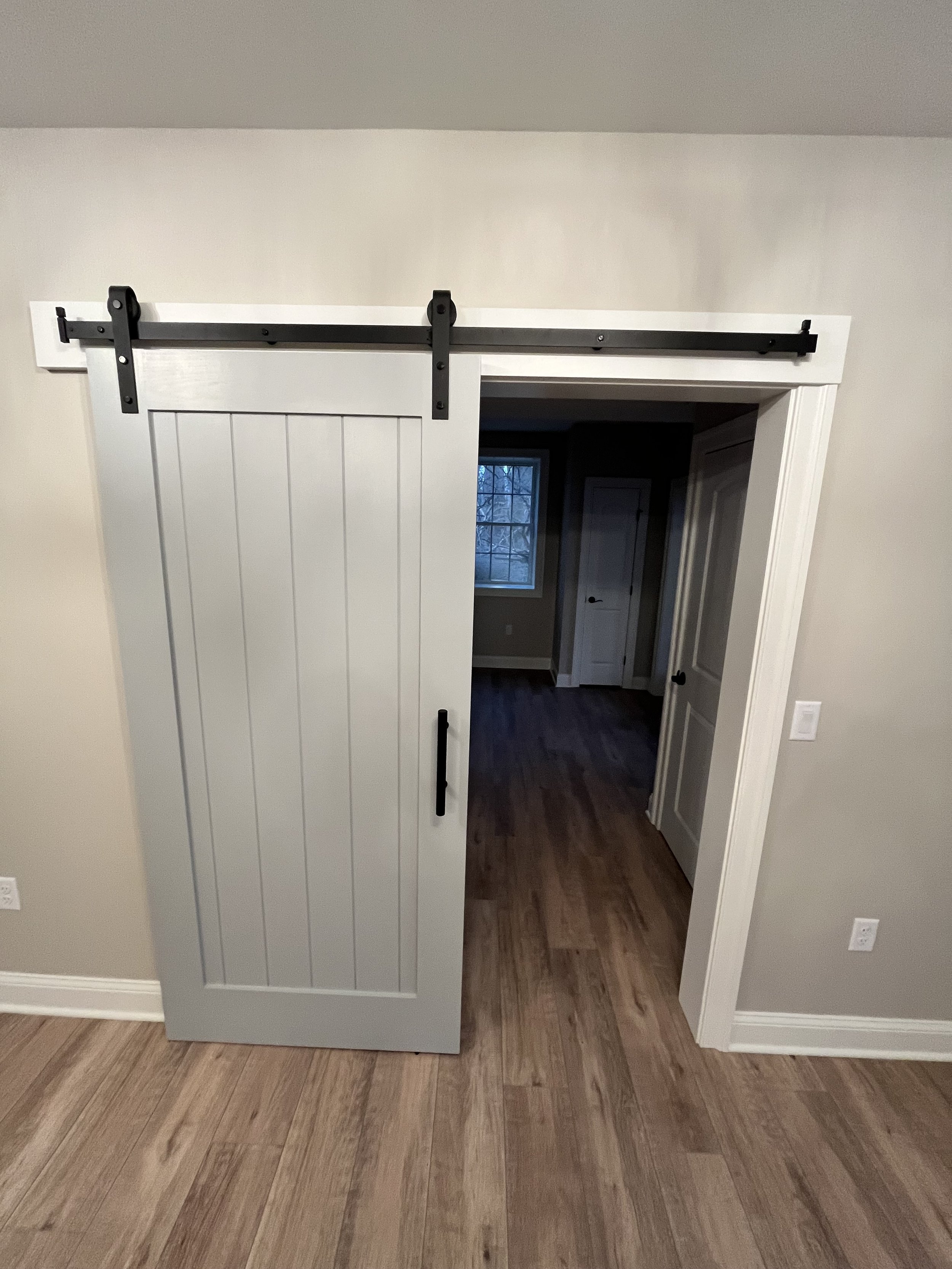 A sliding barn door with black hardware partially open, revealing a room with a window and a closet.