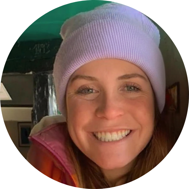 A woman smiling, wearing a light purple beanie and an orange and pink jacket.