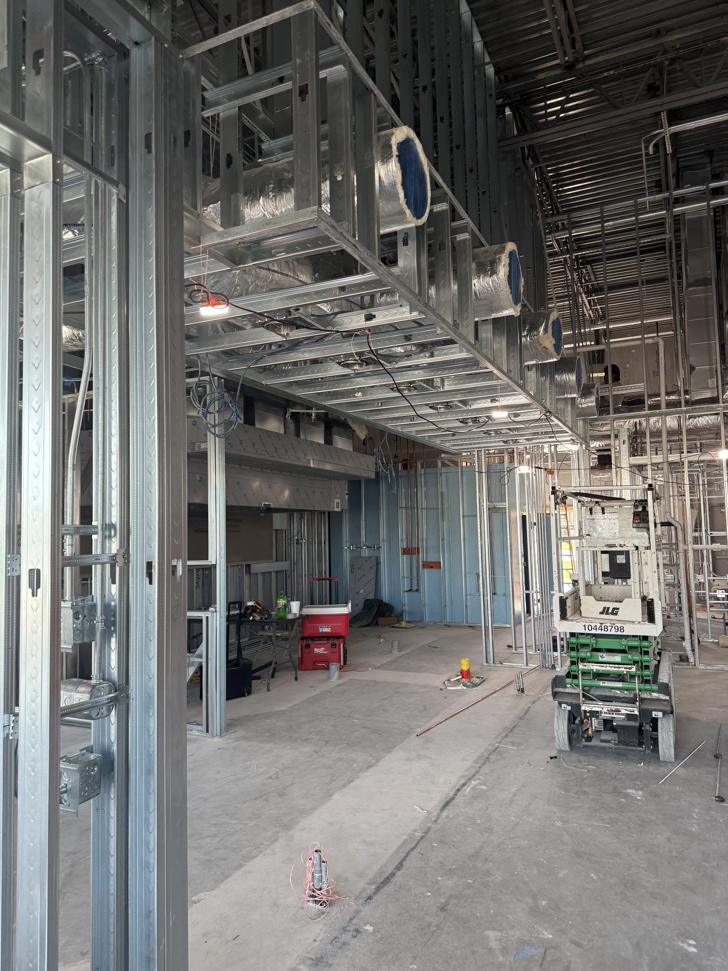Construction site with metal framing, electrical wiring, and a lift in progress.