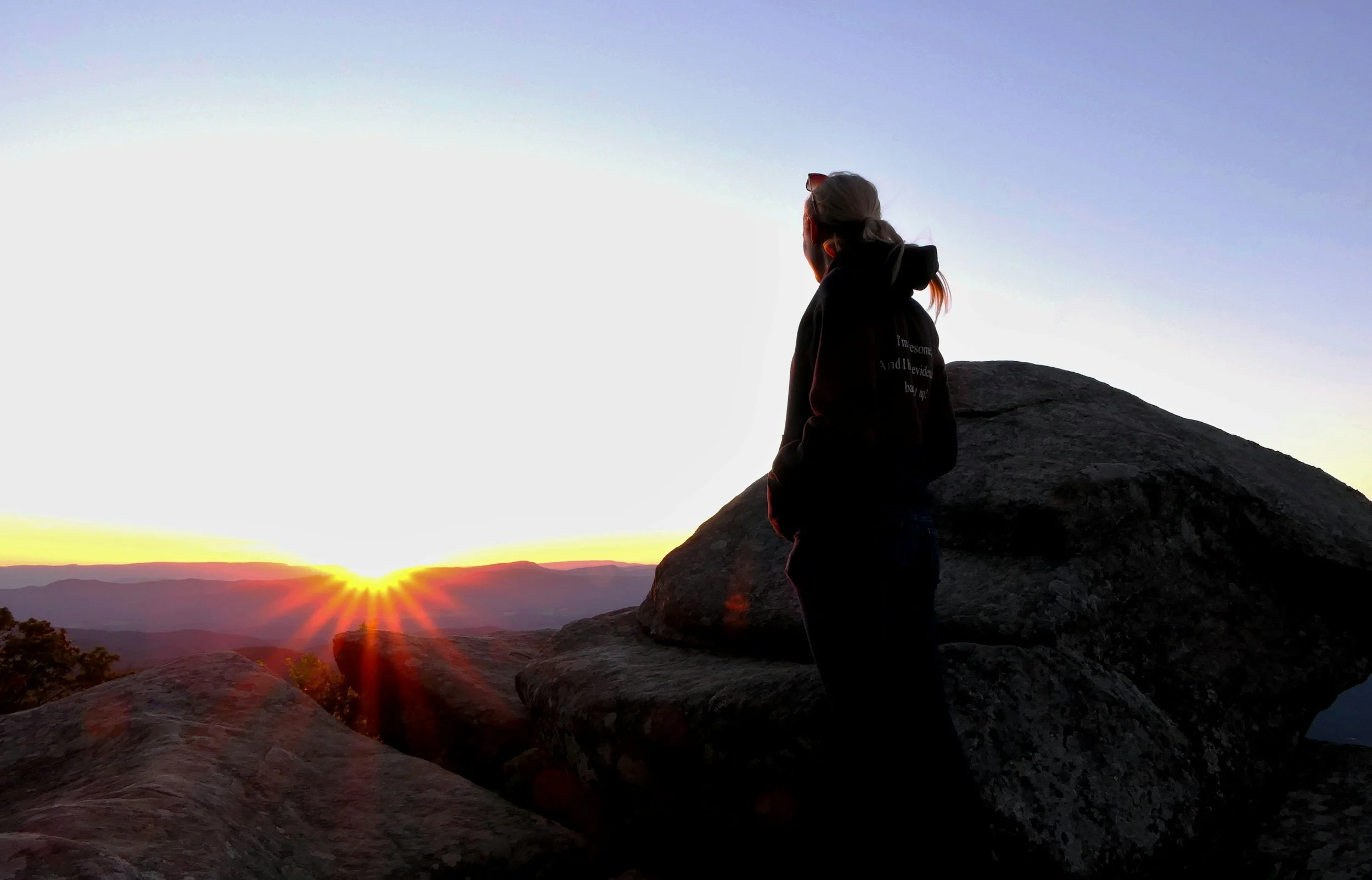 Person standing on rocky cliffs at sunrise, reflecting quietly while overlooking a peaceful mountain landscape, representing healing, self-reflection, and emotional growth at Bountiful Health