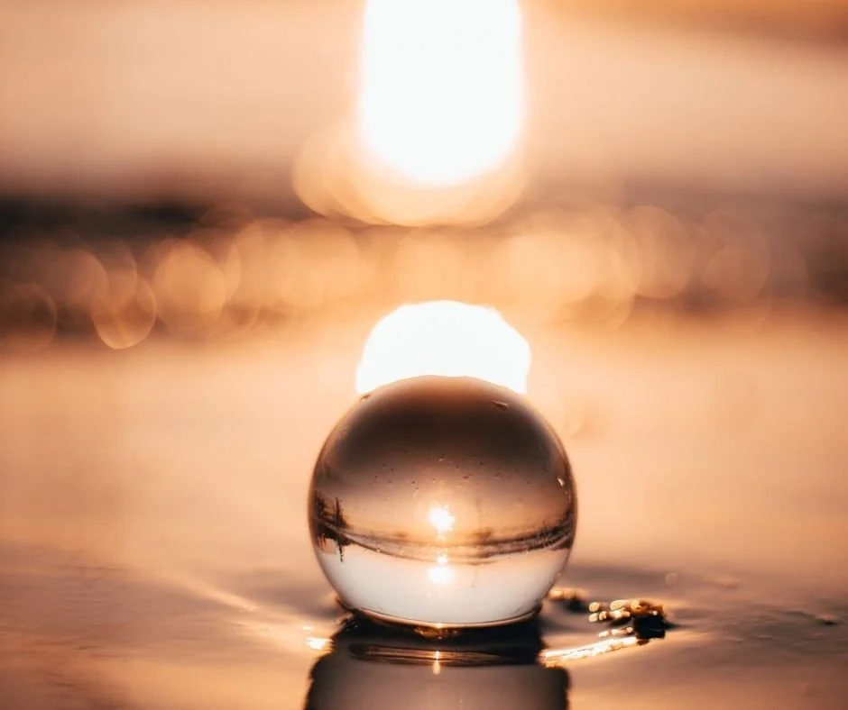 Glass sphere resting on wet sand at sunset, reflecting an inverted image of the horizon, with warm light in the background.