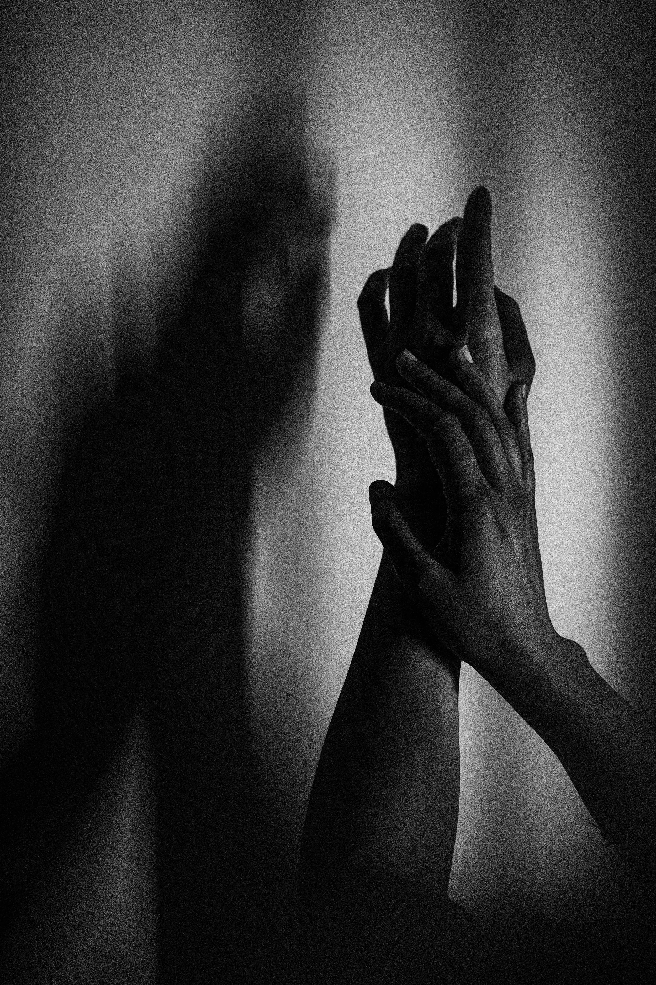 wo hands touching gently, fingers interlaced against a shadowed wall.
