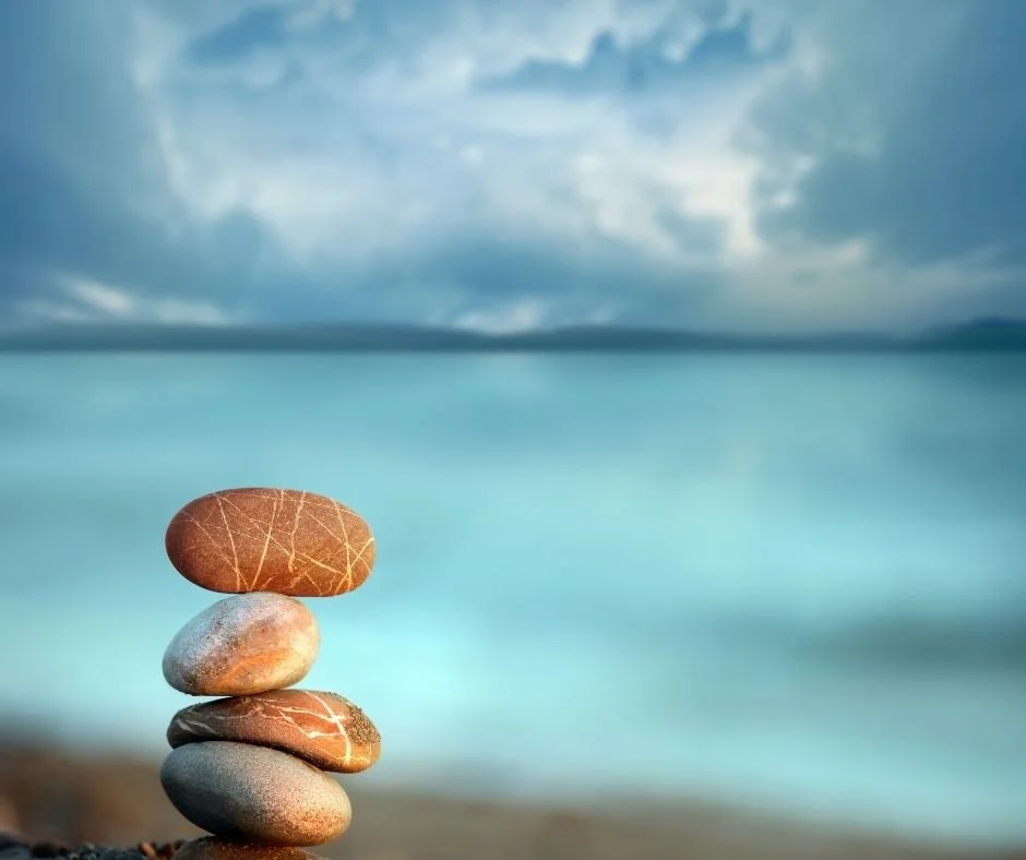 Stacked stones balanced near calm blue water, symbolizing emotional balance and finding the right fit in therapy in Danville.