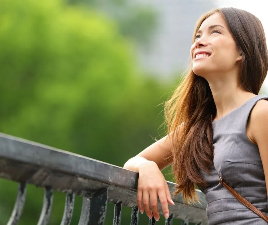 Woman smiling and looking up outdoors, representing the relief and hope that can come after therapy for relationship patterns.