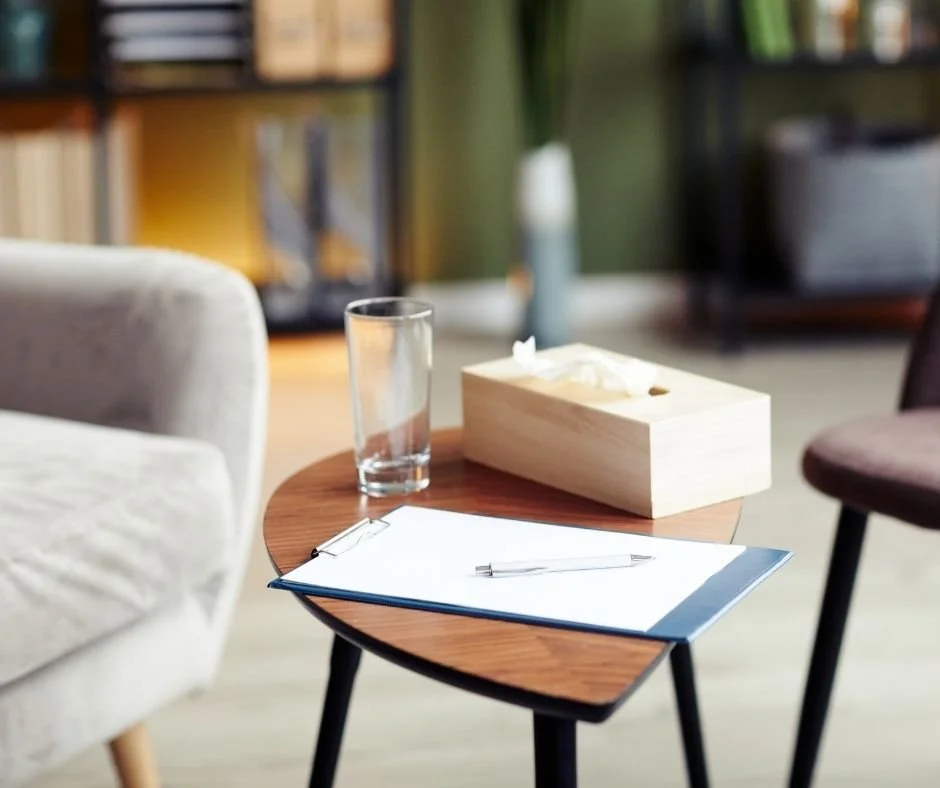Comfortable therapy office with a clipboard, pen, water glass, and tissues on a table, creating a calm setting for therapy in Danville.