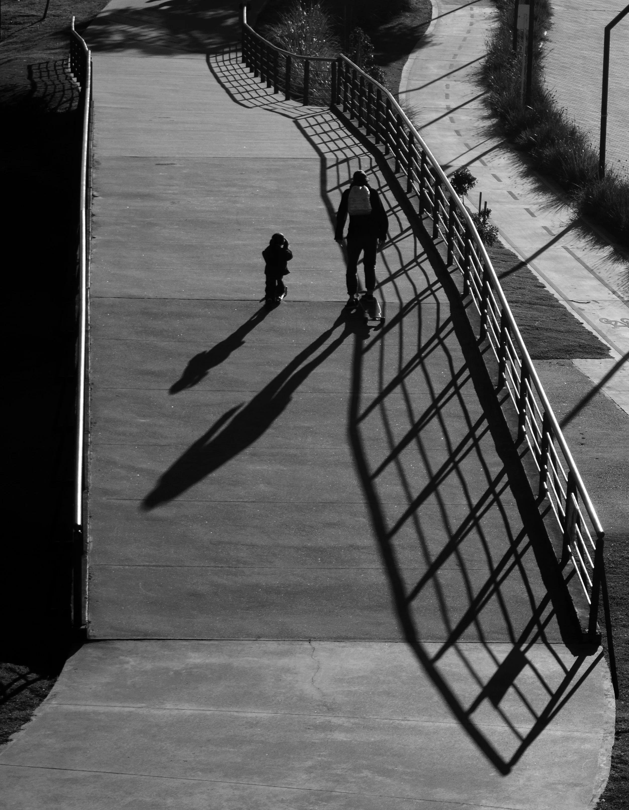 Two silhouetted figures walking along a bridge, one following closely behind, casting long shadows.