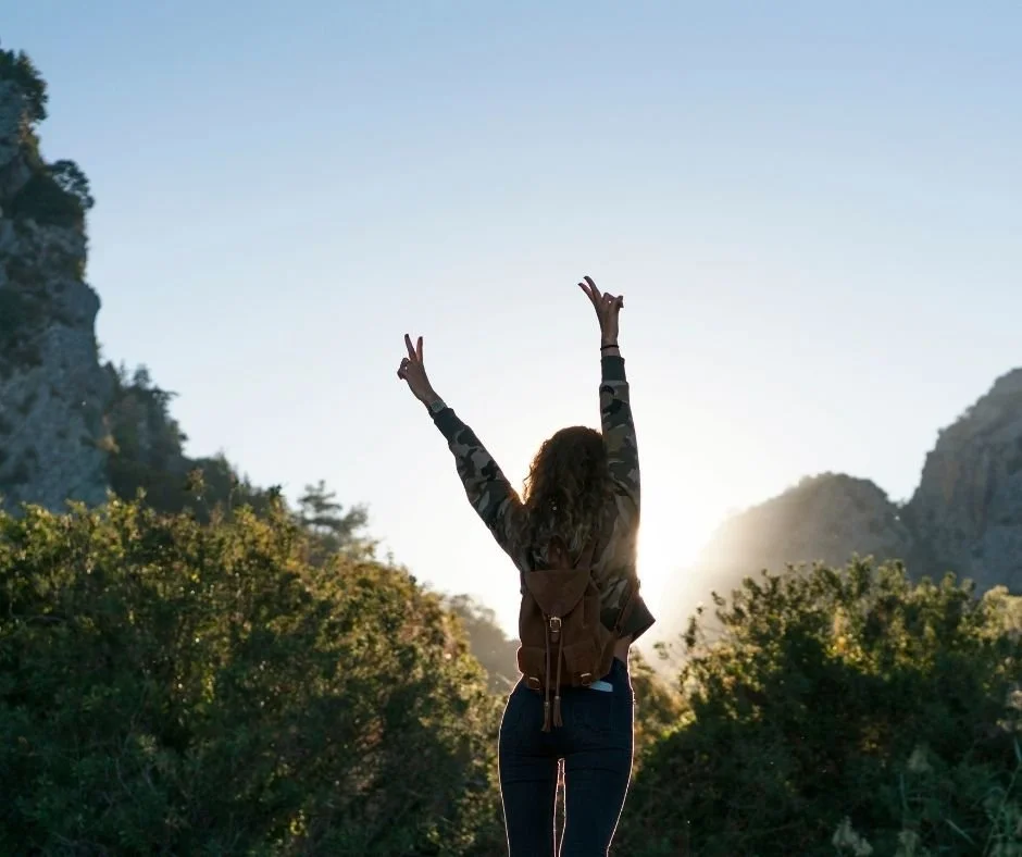 Woman raising her arms in celebration on a mountain trail, representing freedom, empowerment, and personal growth after therapy.