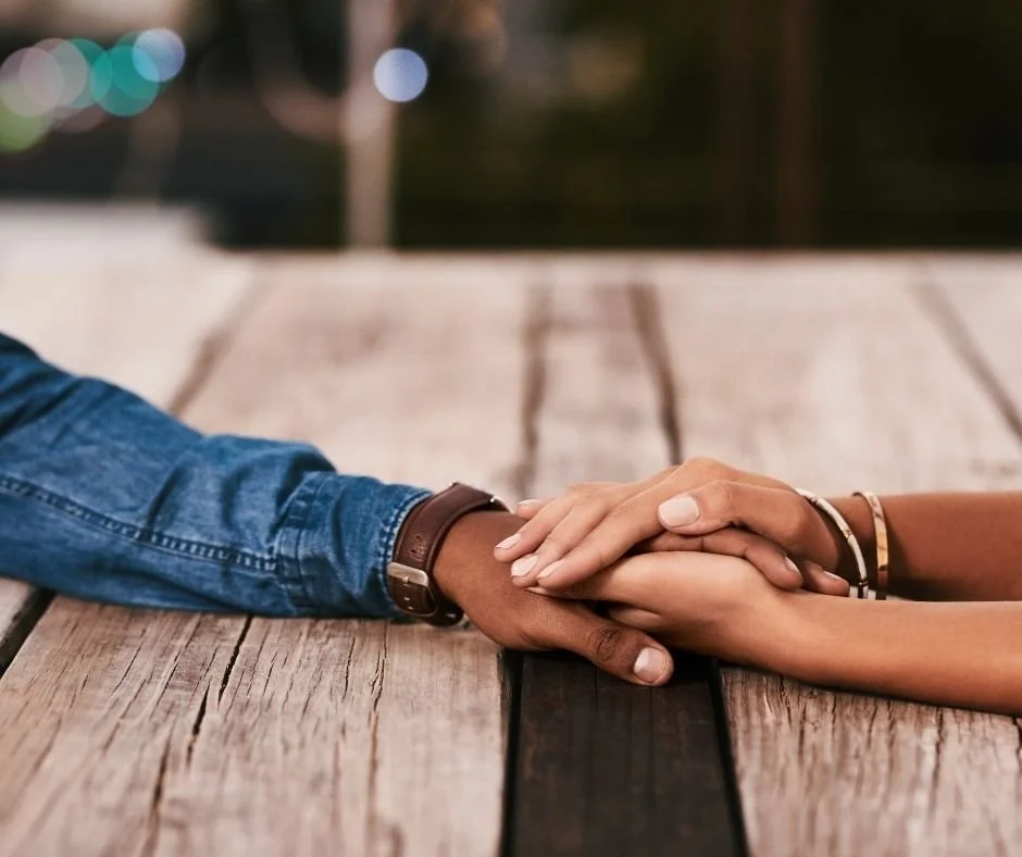 Two people holding hands across a wooden table, representing trust and connection in relationship therapy in Orinda, CA.