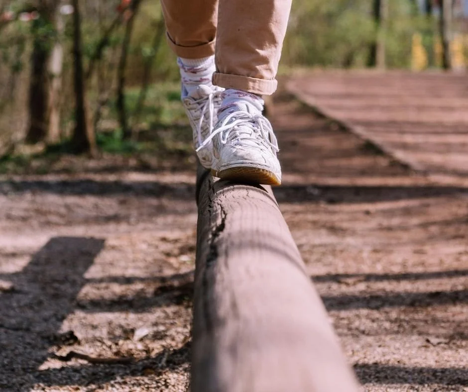 Person balancing on a wood beam outdoors.