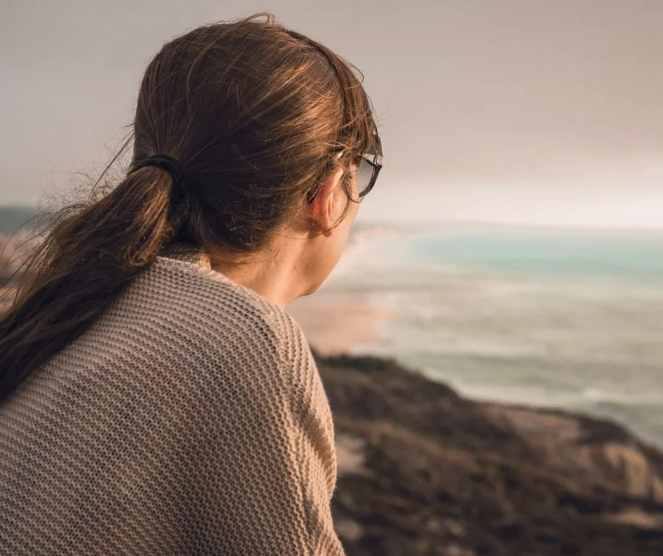 Woman looking out over the ocean in quiet reflection, representing self-reflection and personal growth in therapy in Orinda, CA.