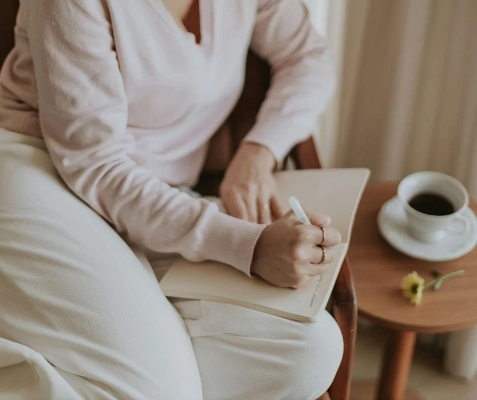 Close-up of a woman writing in a journal in a cozy chair with coffee nearby, therapy in San Ramon, CA