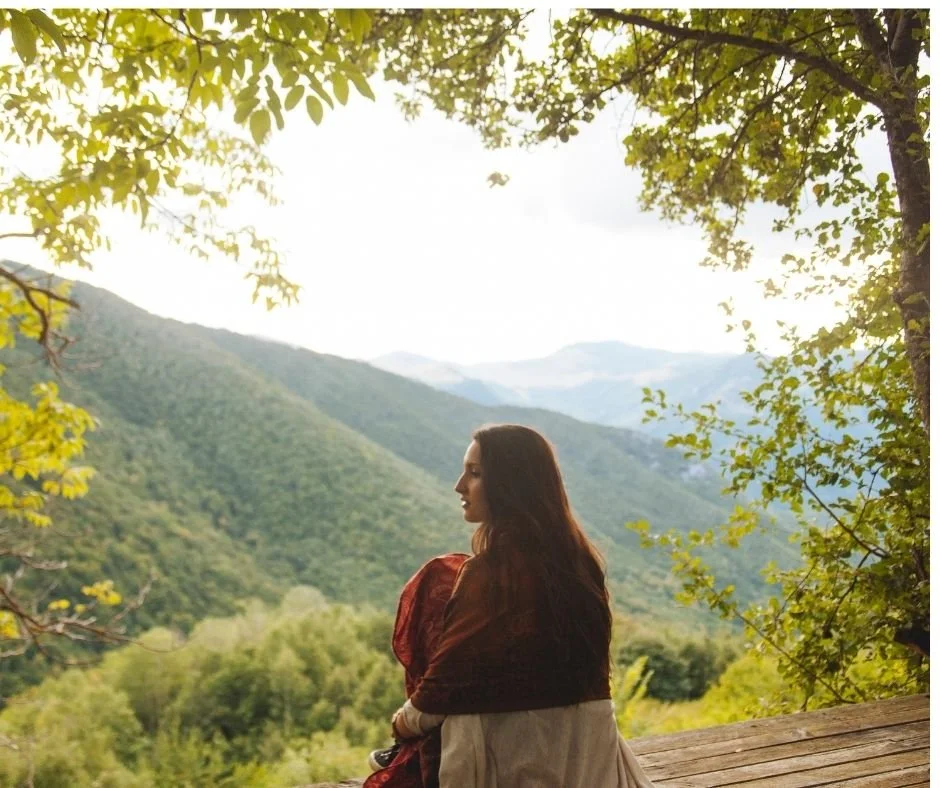 Woman sitting quietly overlooking a mountain valley, representing stillness and reflection on the therapy journey.