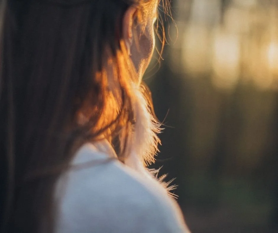 Woman turned away, hair catching the last light of golden hour.