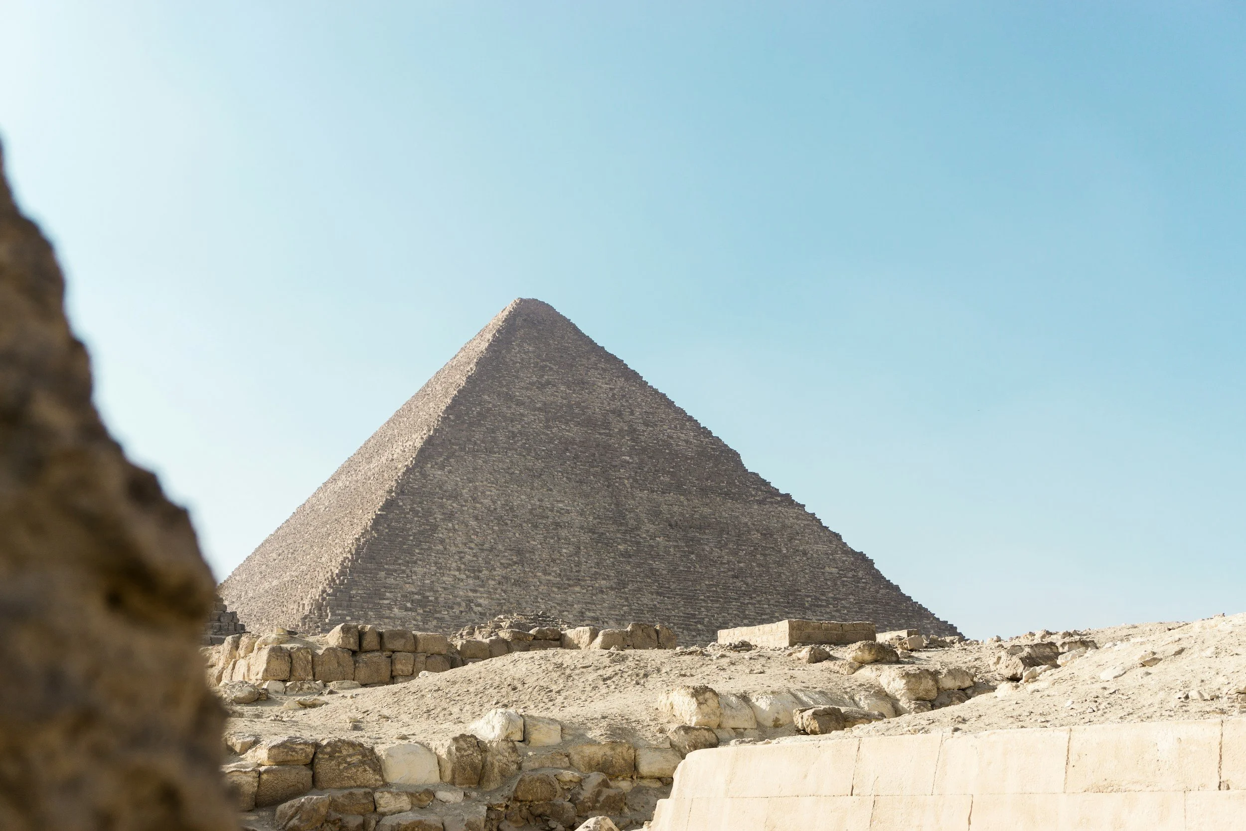 Photo of the Great Pyramid of Giza in Egypt, showing its stone blocks and sandy surroundings under a clear blue sky.