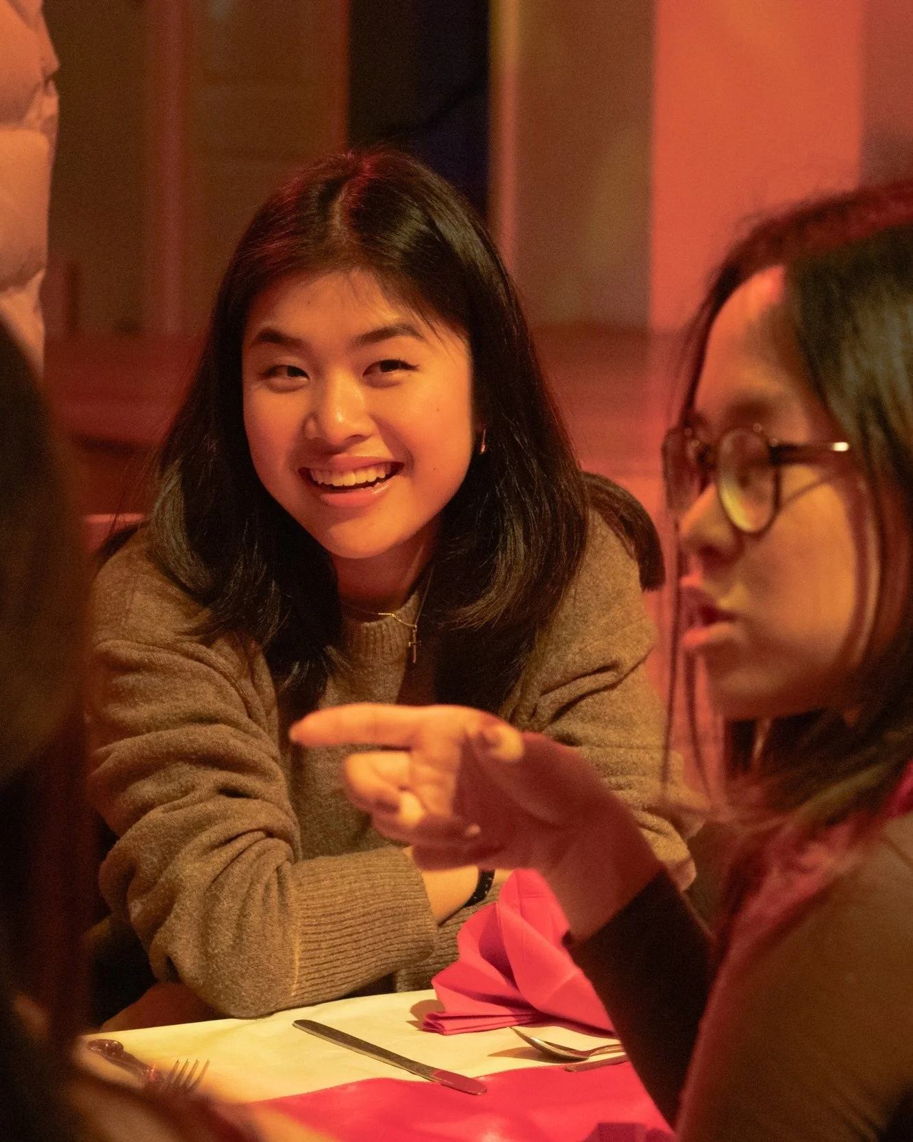 Group of people having a conversation at a restaurant table with red napkins and utensils.