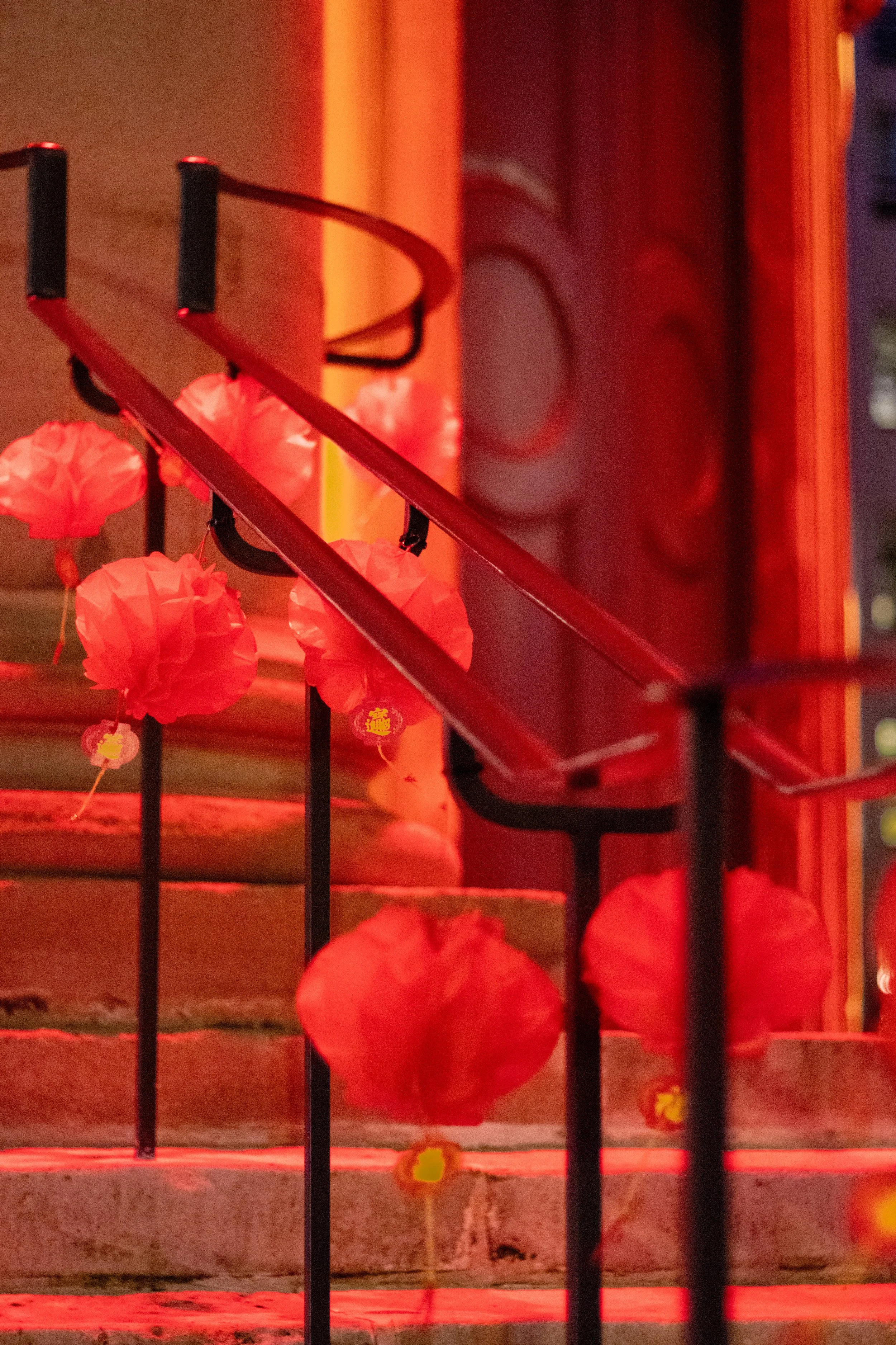 Red lanterns hanging on a staircase with metal railings, illuminated by red lighting.