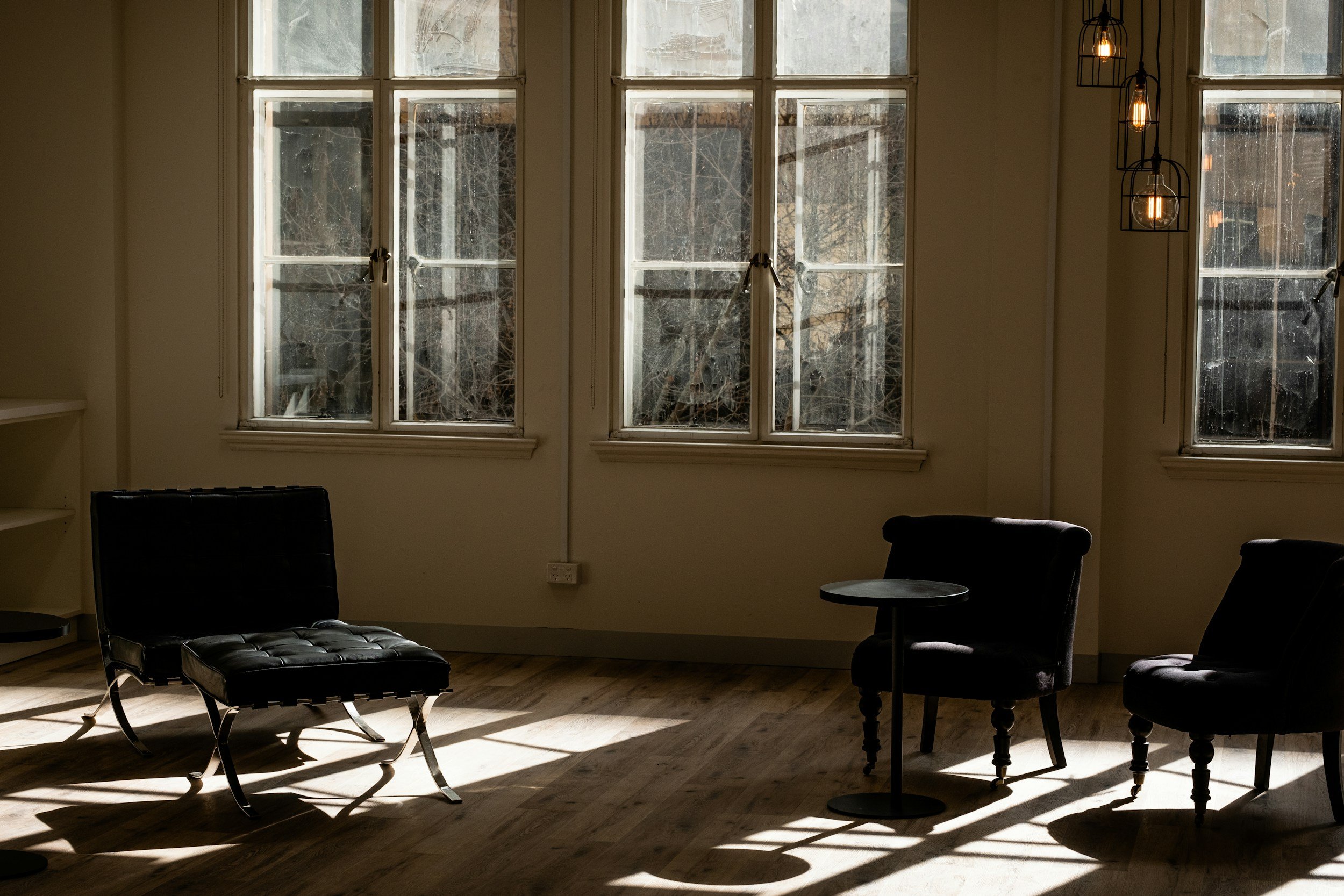 Sunlight streaming through tall windows onto minimalist chairs in a calm, neutral-toned therapy room — reflecting the warm, grounded environment of Gradients Counseling.